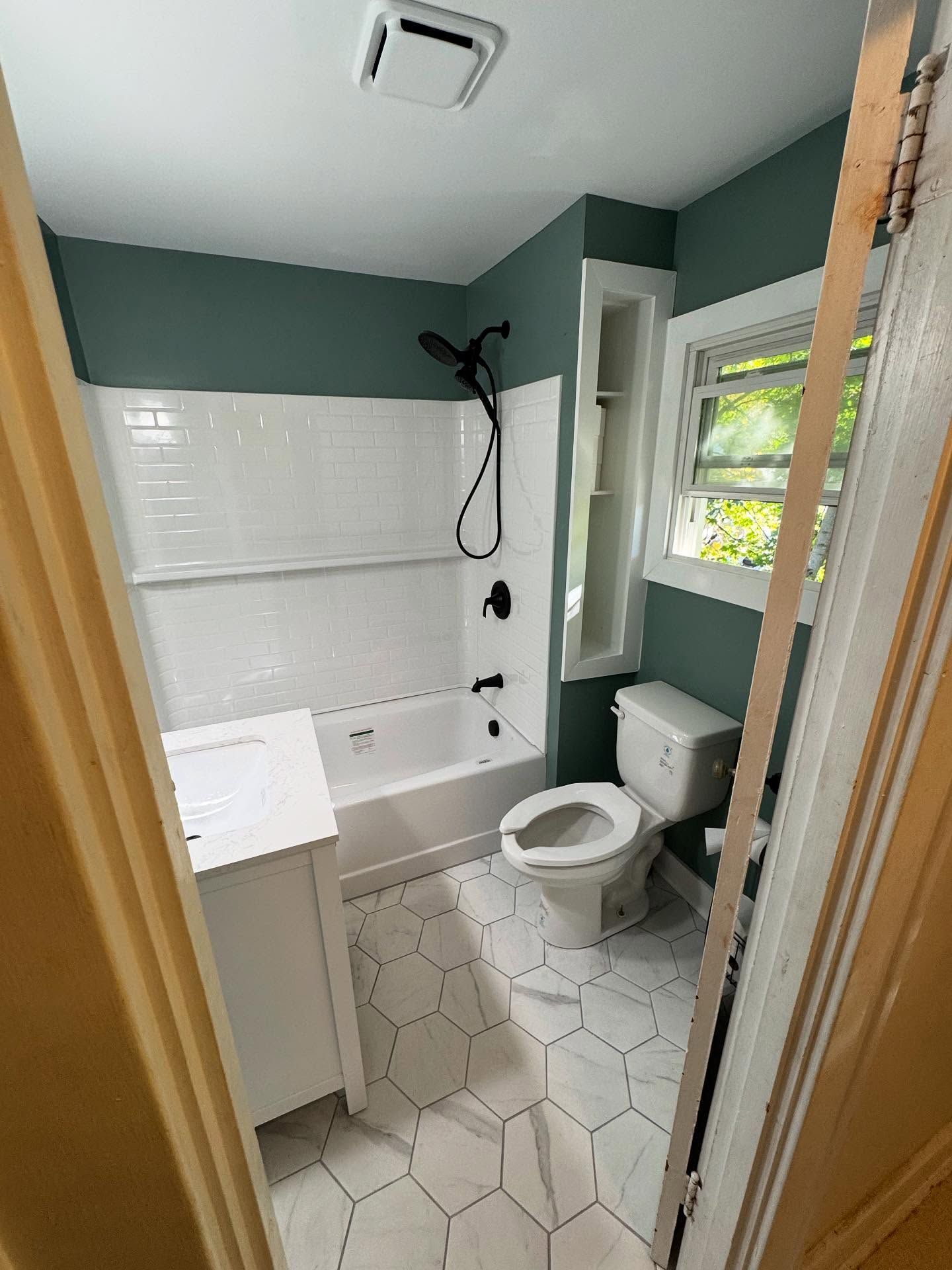 Bathroom with white fixtures, teal wall, and hexagon tile floor. Black showerhead.