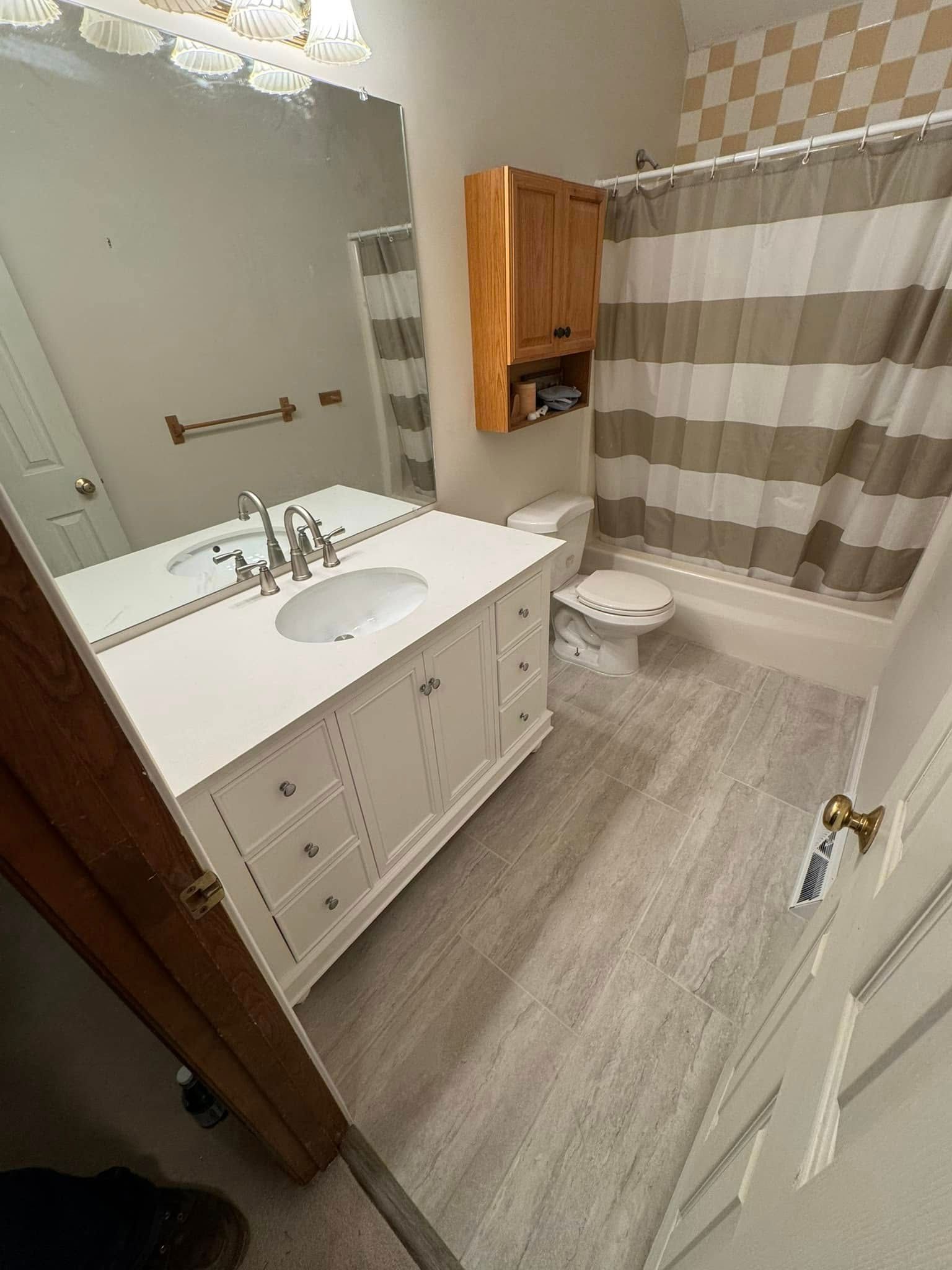 Bathroom with white vanity, toilet, and beige/white striped shower curtain. Light gray floor.