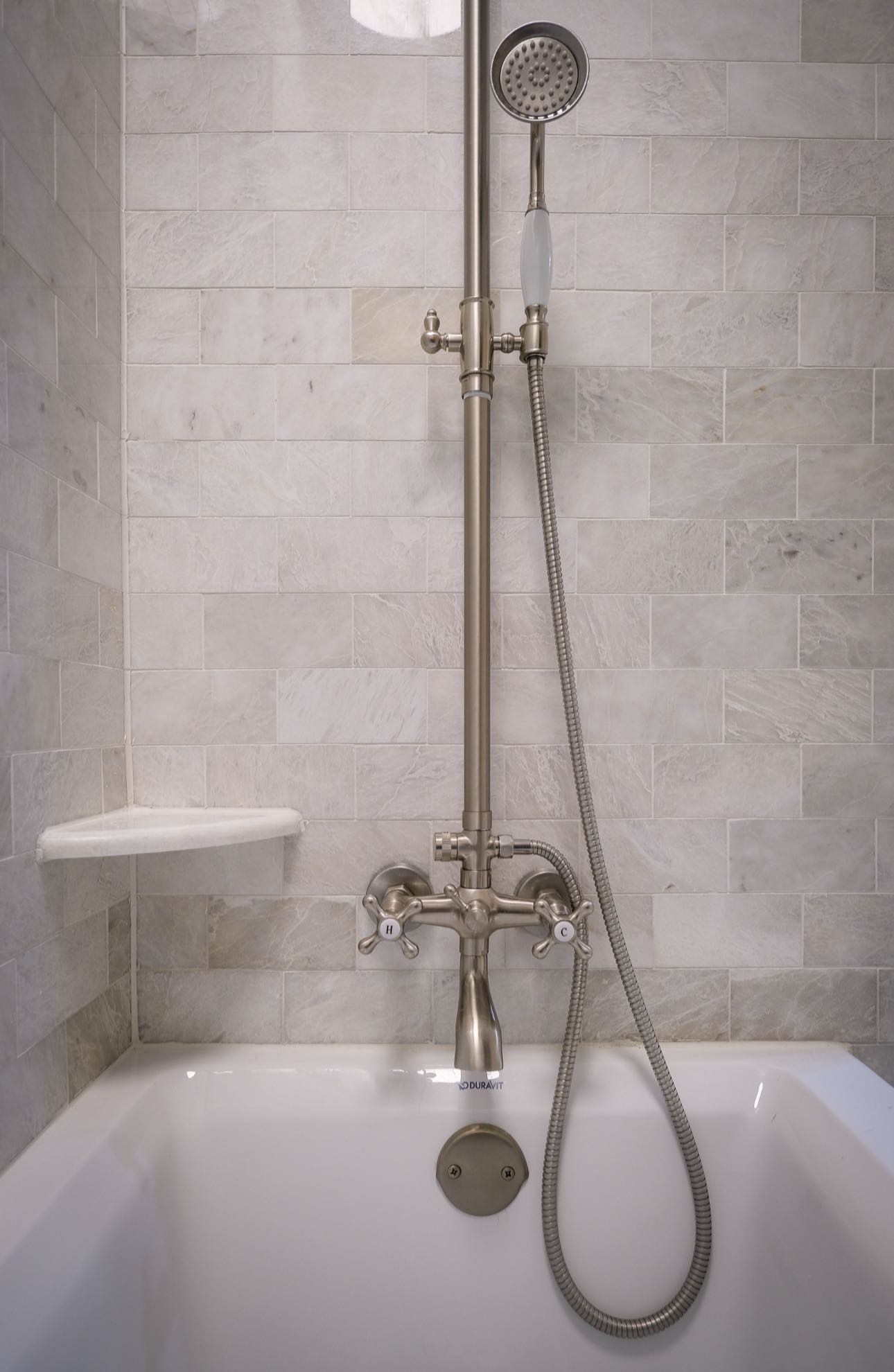 Bathtub with a silver showerhead, faucet, and stone tile backdrop.