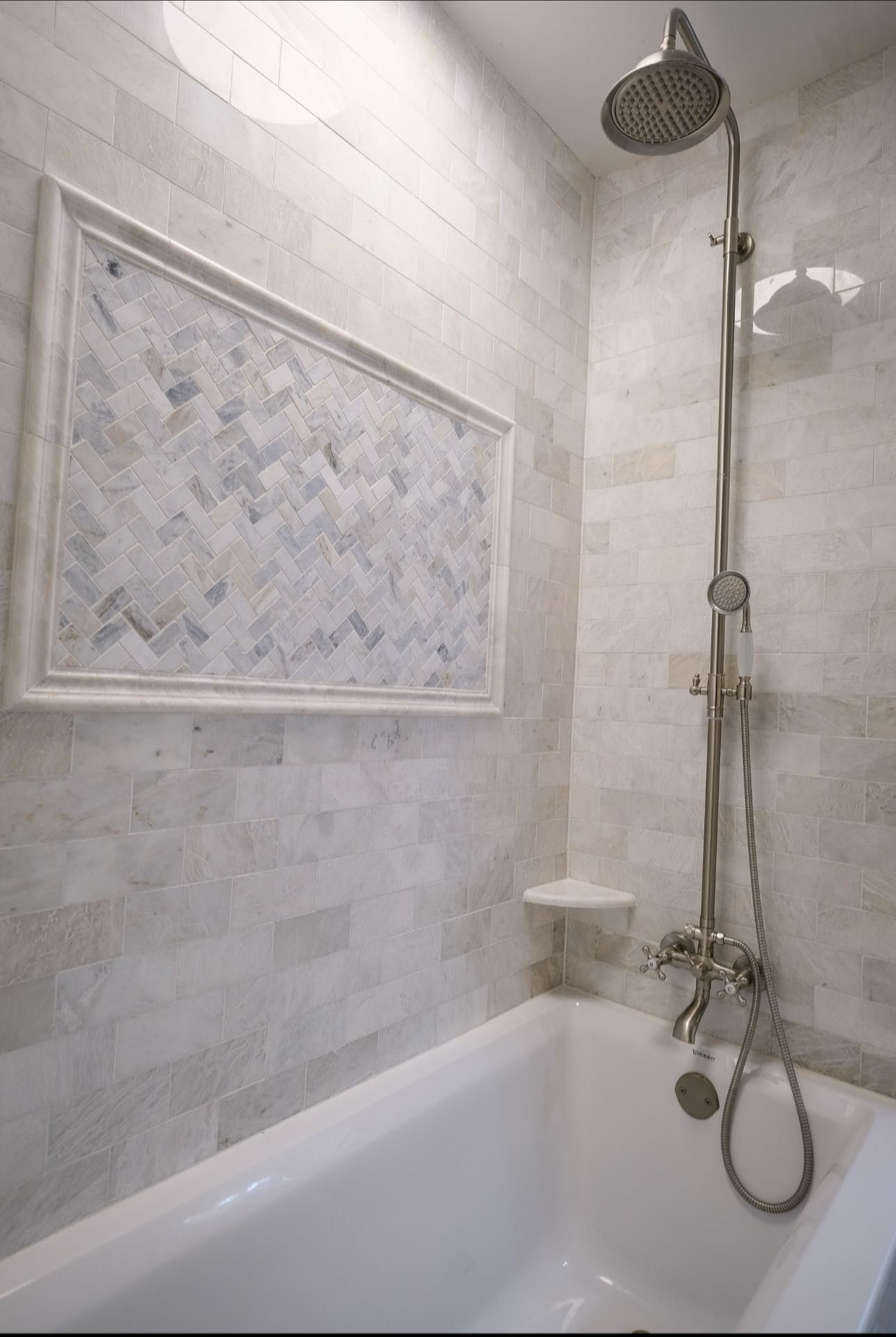 Bathroom with white tub, shower head, and tiled walls with a decorative inset.