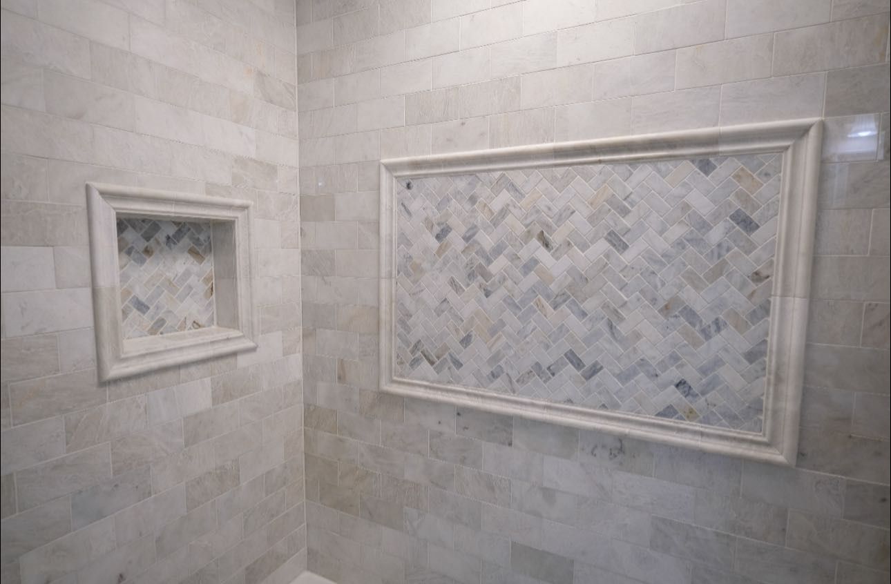 Bathroom with light stone tile walls, a built-in shelf, and a framed mosaic tile accent.