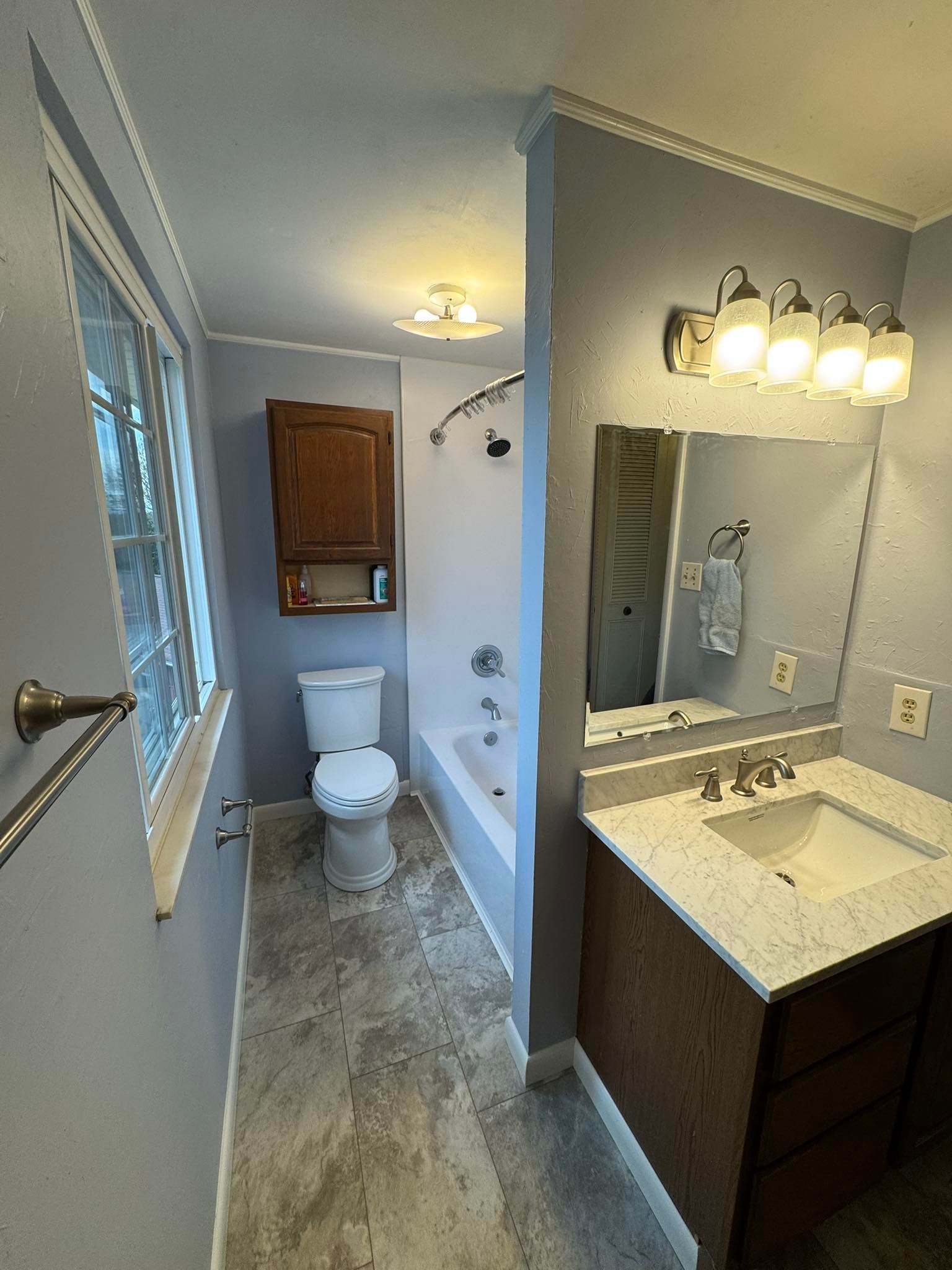 Bathroom with light blue walls, vanity, toilet, and a shower/tub combo.