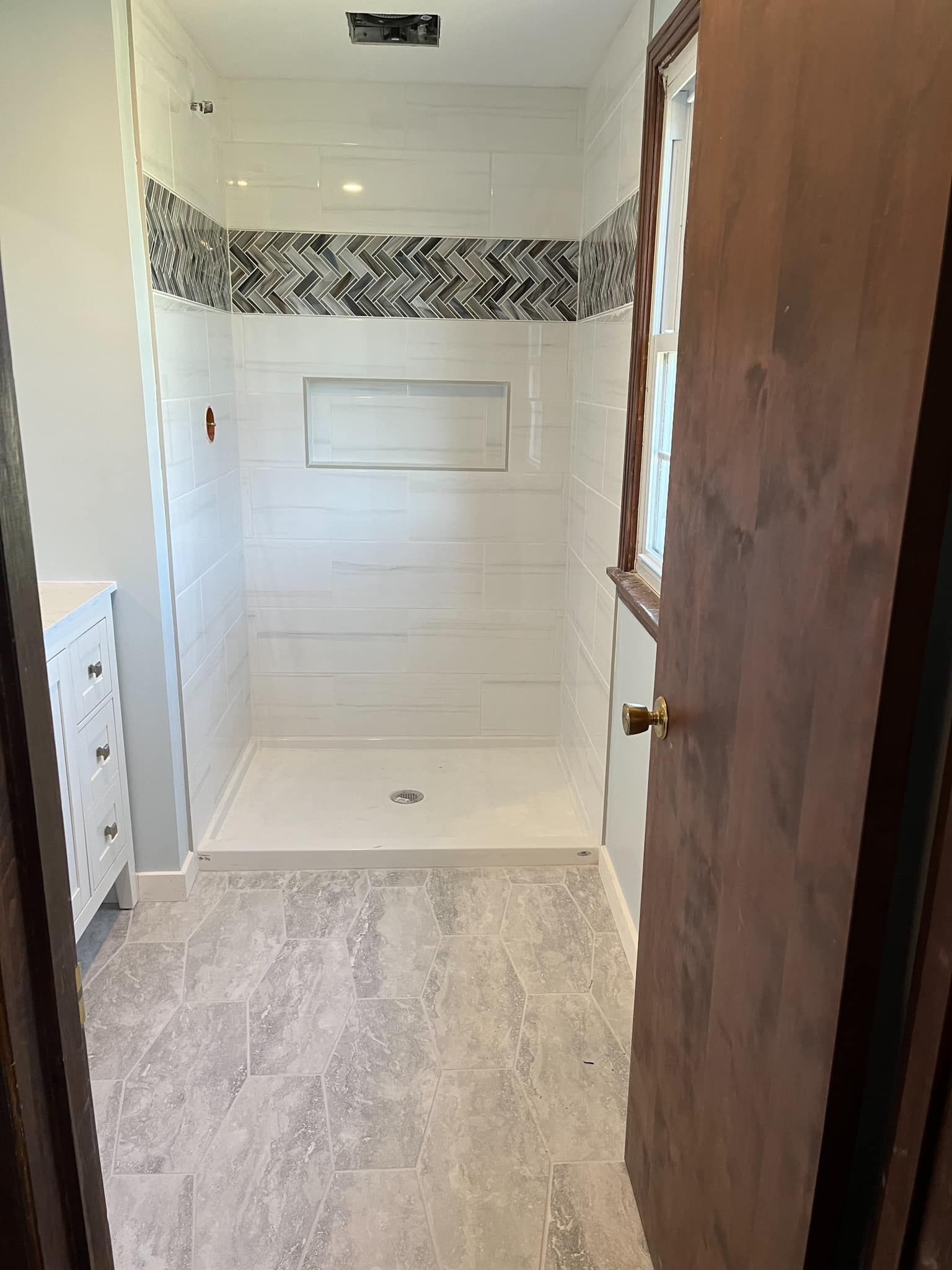 Newly renovated white shower with decorative tile, recessed shelf, and gray tile floor.
