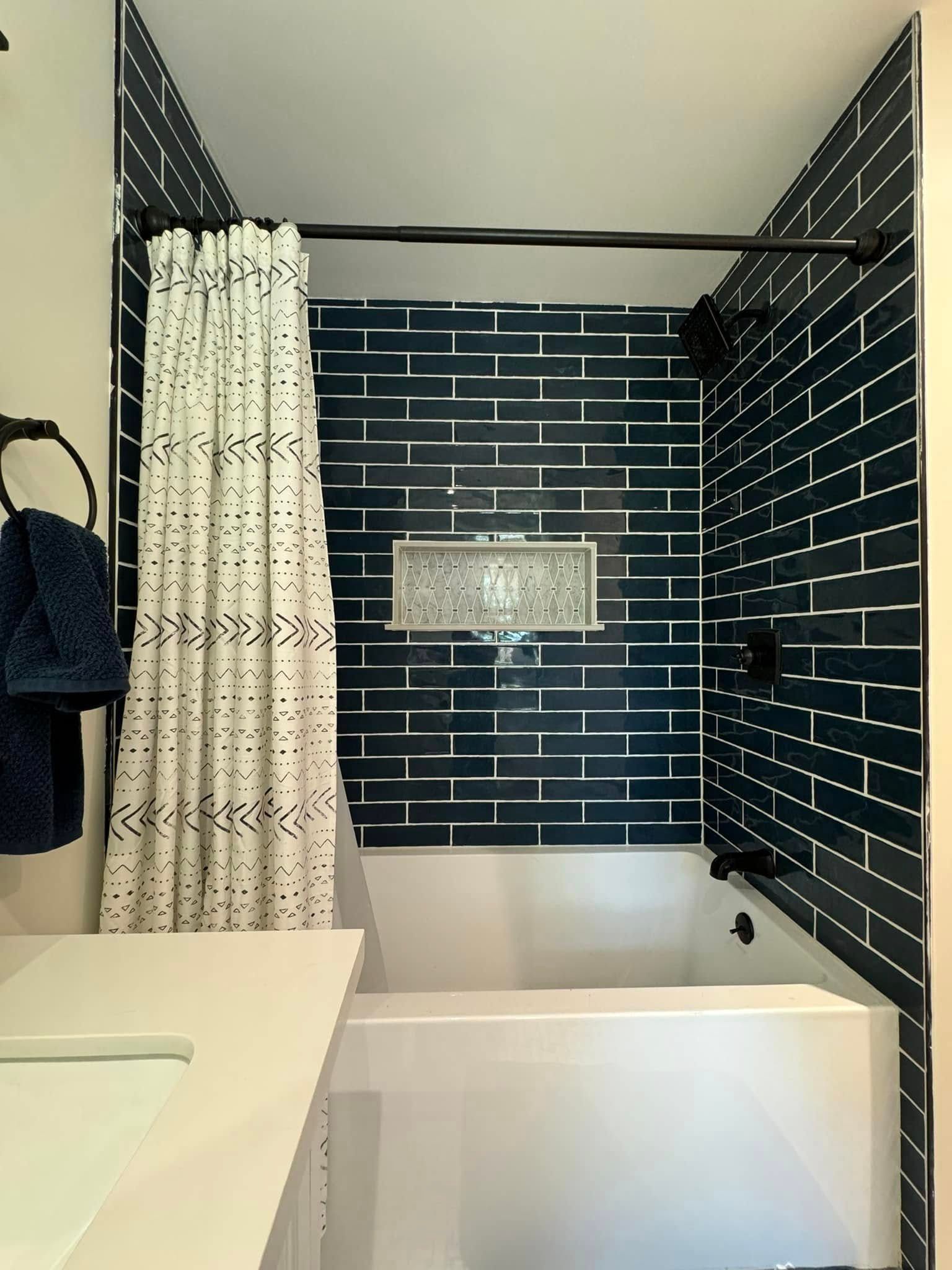 Blue tiled shower with a white tub, shower curtain, and dark fixtures.