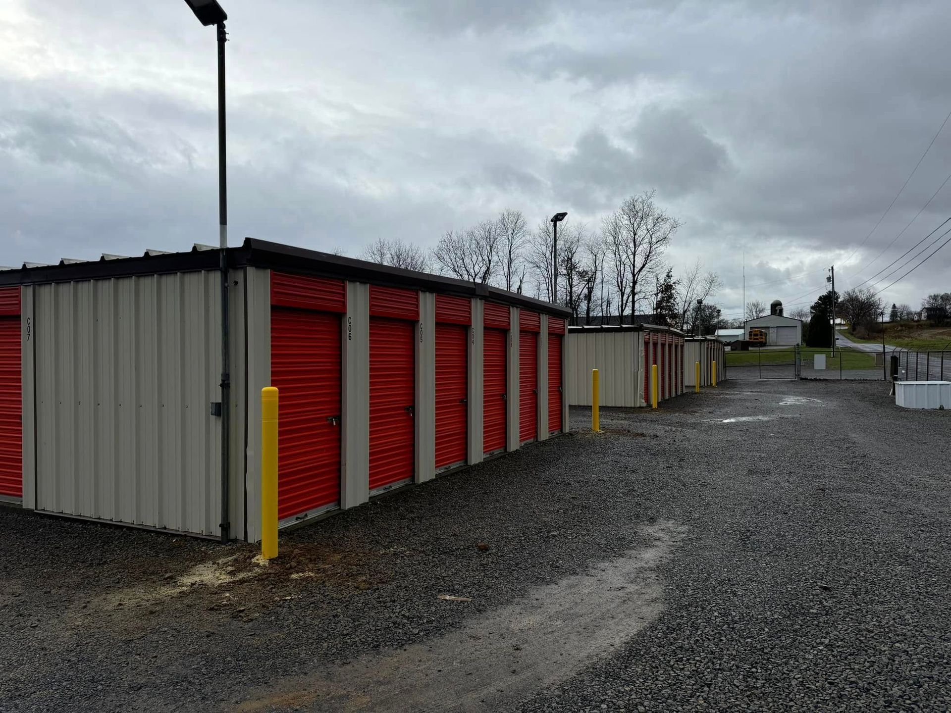 Storage units with red doors, gravel driveway, overcast sky.