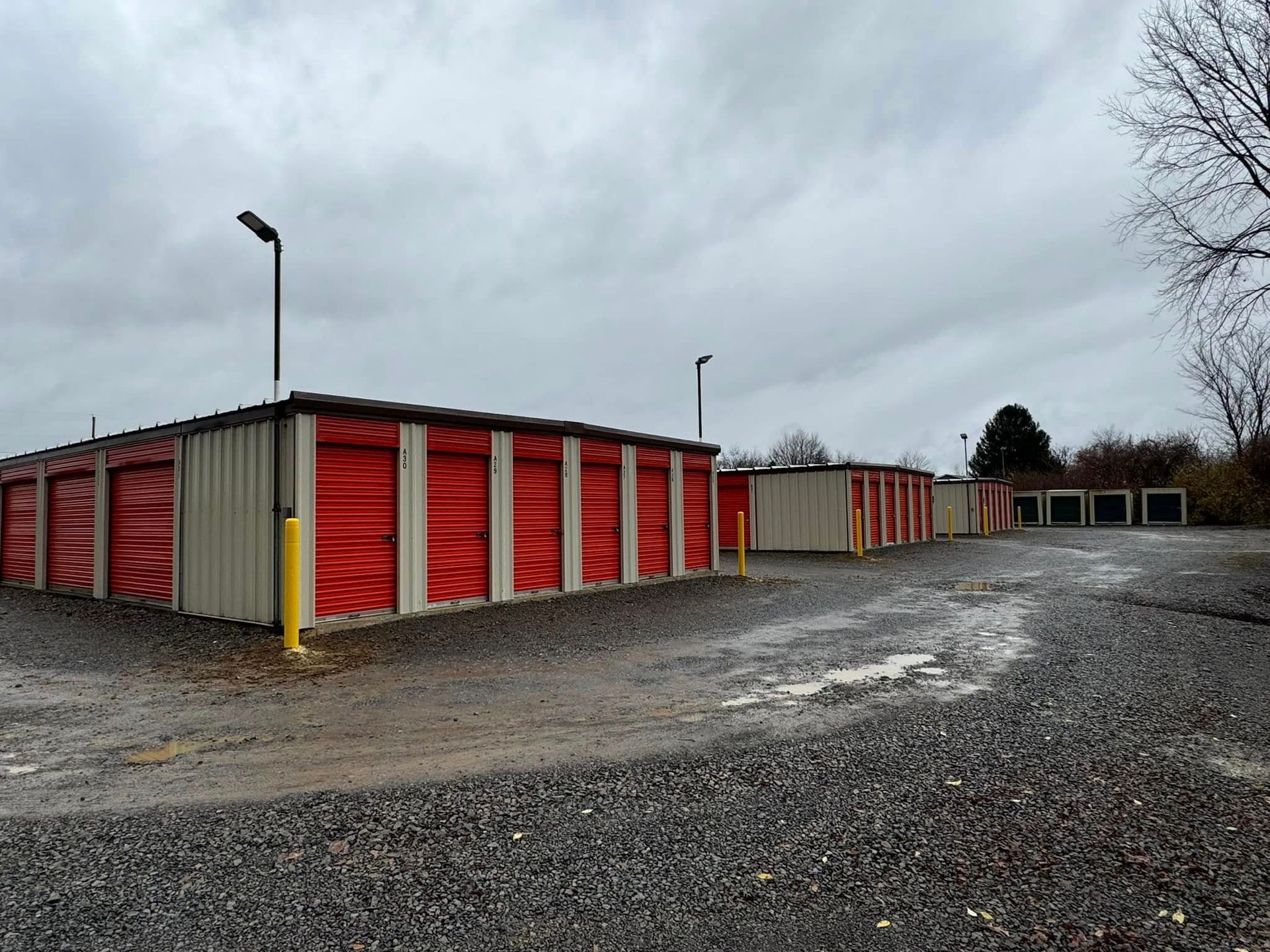 Storage units in a gravel lot on an overcast day. Red doors and tan walls.