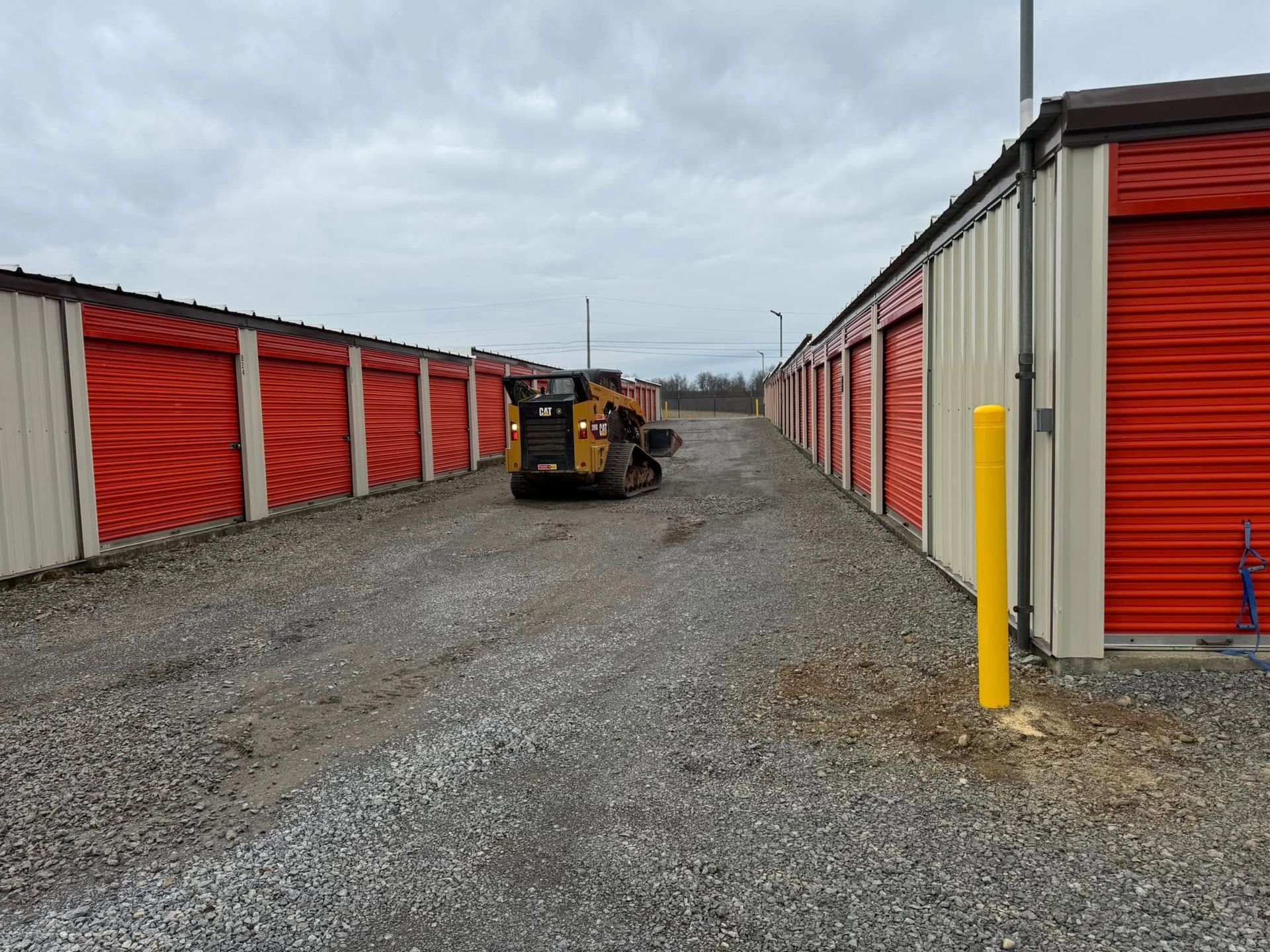 Rows of red storage unit doors; small construction vehicle driving on gravel path.