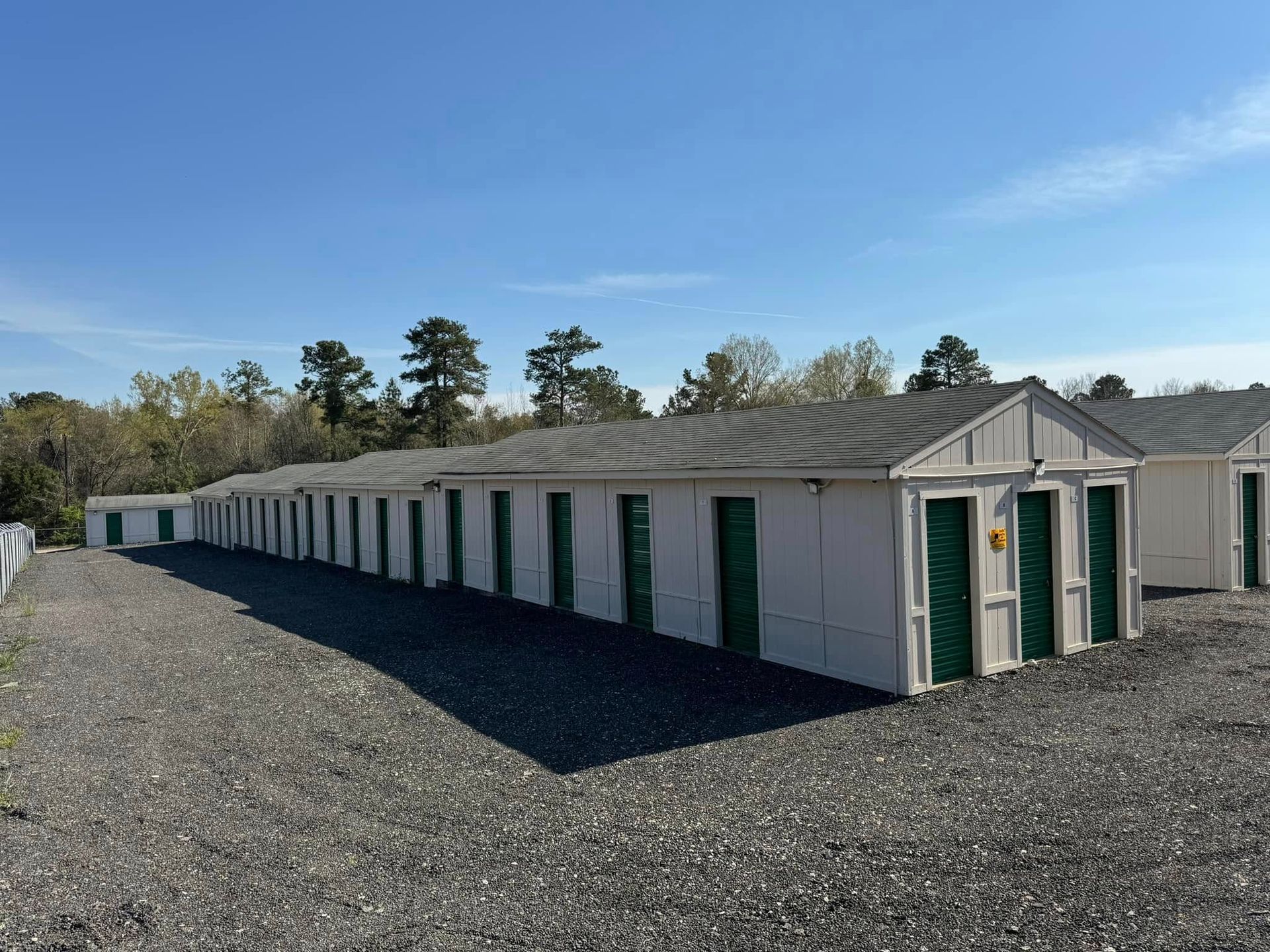 Row of white storage units with green doors under a blue sky.