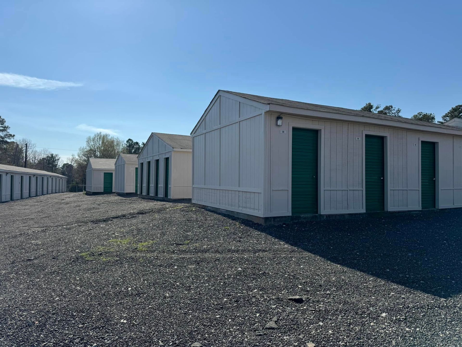 Storage units with green doors and gray gravel ground. Blue sky.