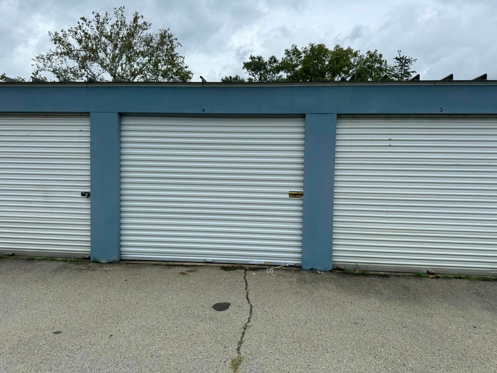Three blue and white storage units with rolling doors under a cloudy sky.