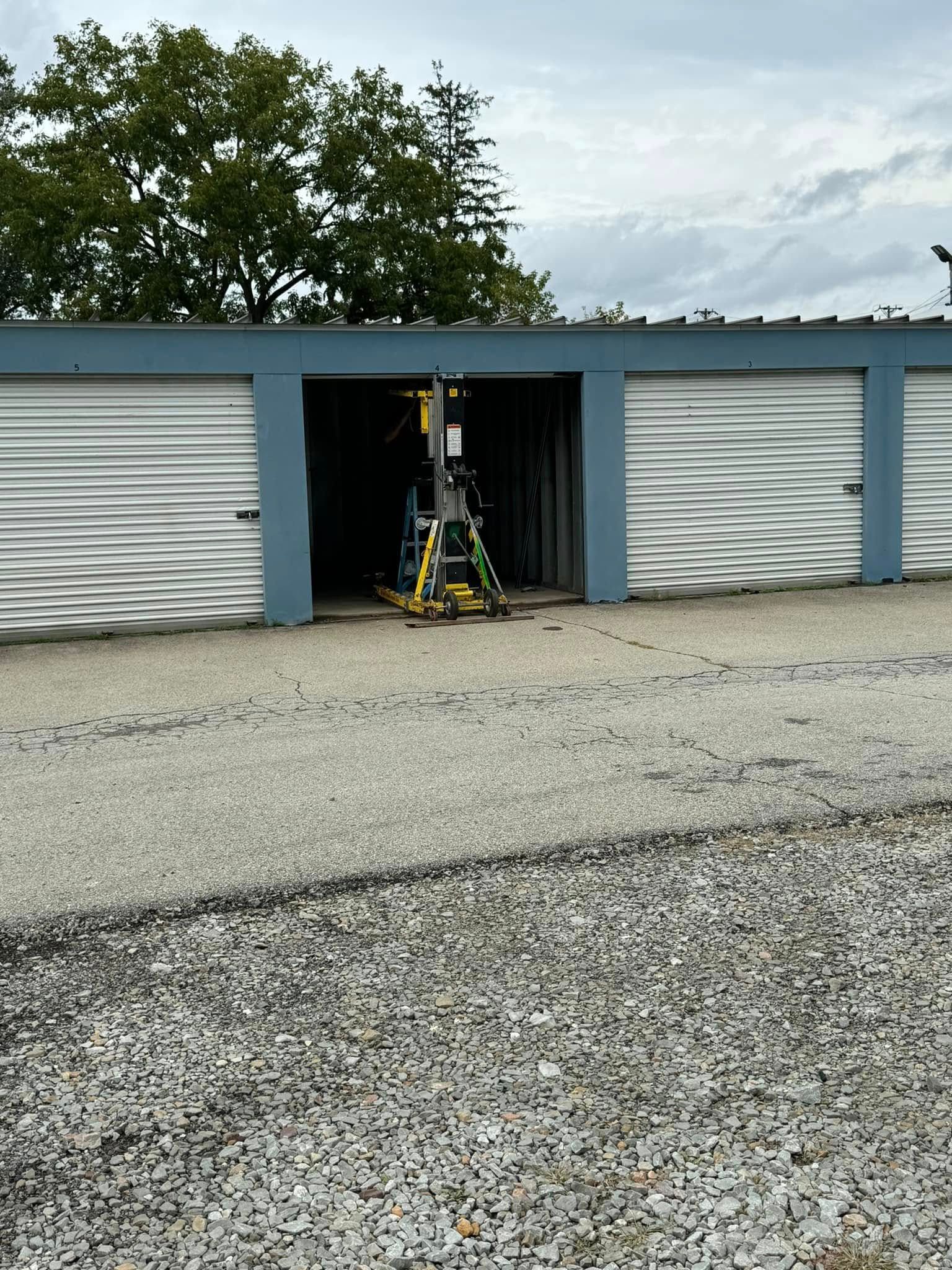Storage units with a unit open, showing equipment and tools inside. Gray and blue exterior.