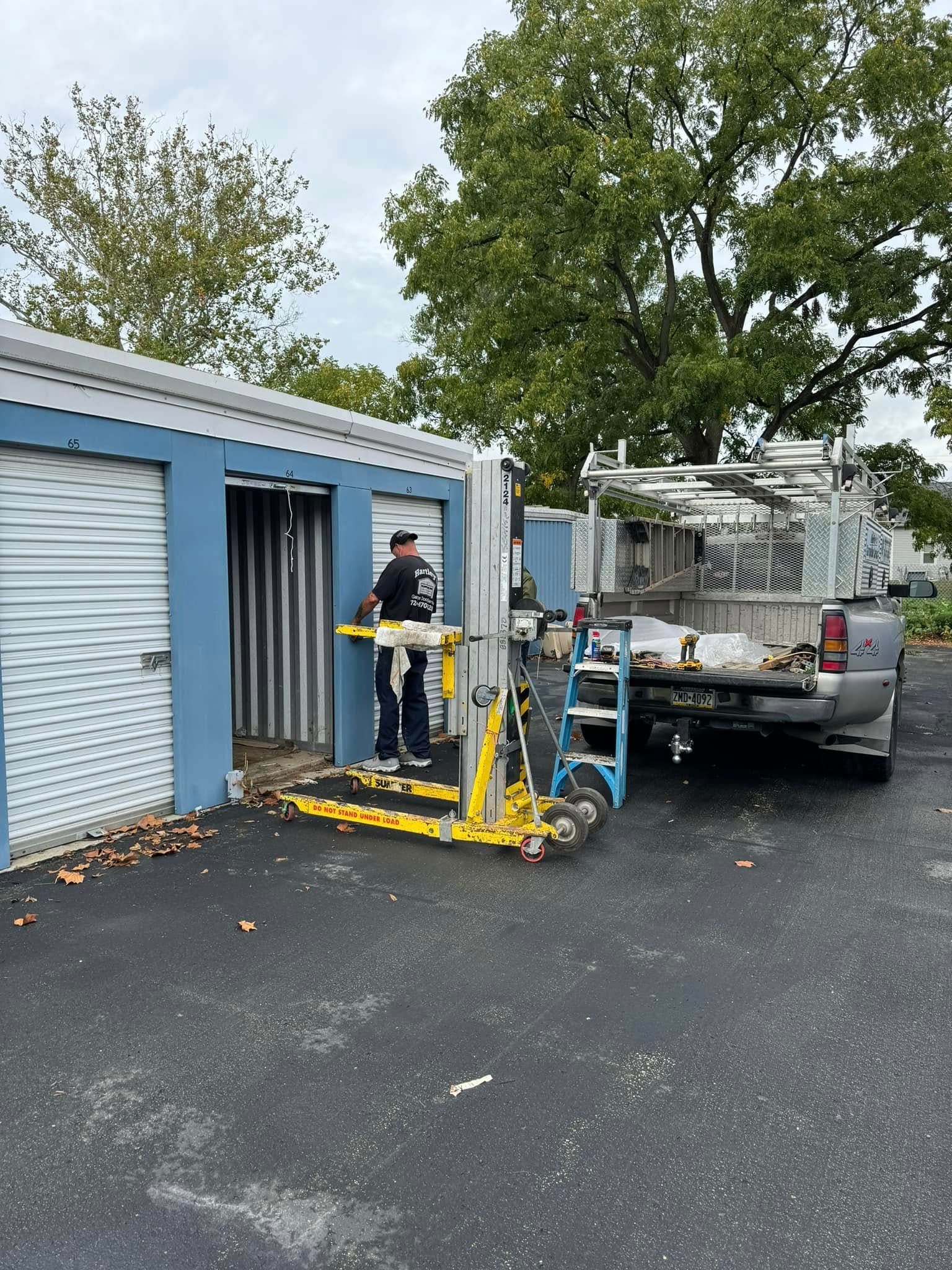 Man loading a storage unit with a forklift next to a truck. Blue unit, gray truck, asphalt lot.