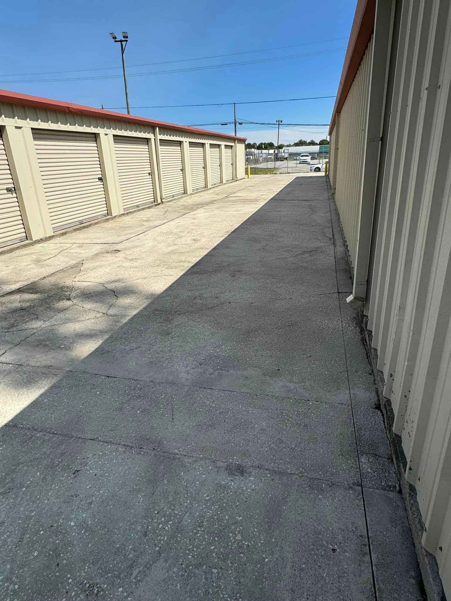 Storage units with light beige doors and a gravel path. A dark gray asphalt path runs along the right side.