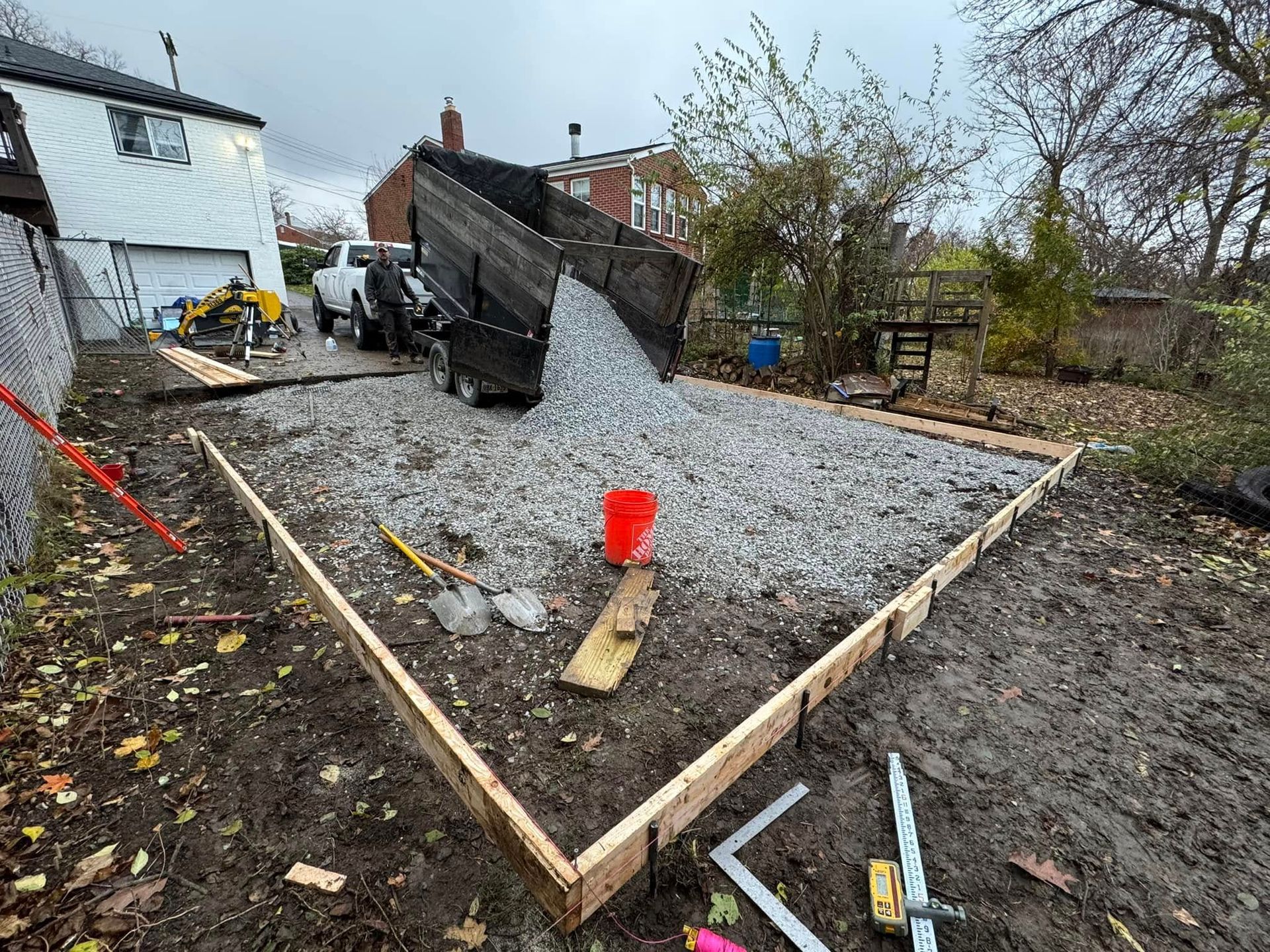 A dump truck unloading gravel into a framed area for a construction project in a backyard.