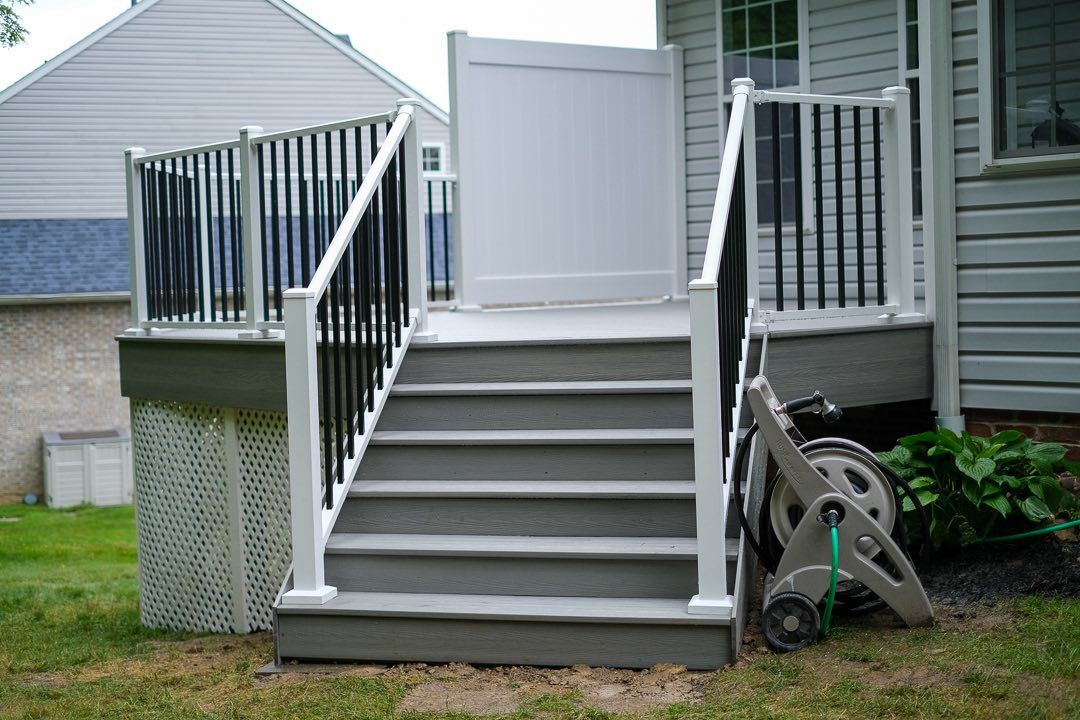 Gray deck stairs with white and black railings leading to a white gate. Hose reel on the right.