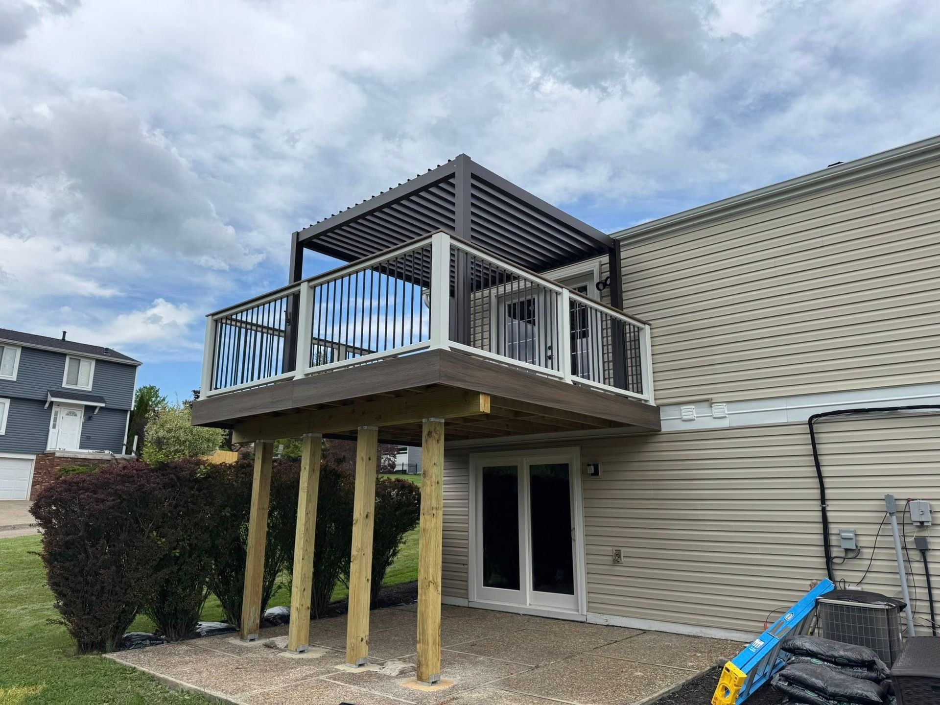 Deck with pergola and railing, attached to a house. Wooden supports and a gravel patio are visible.