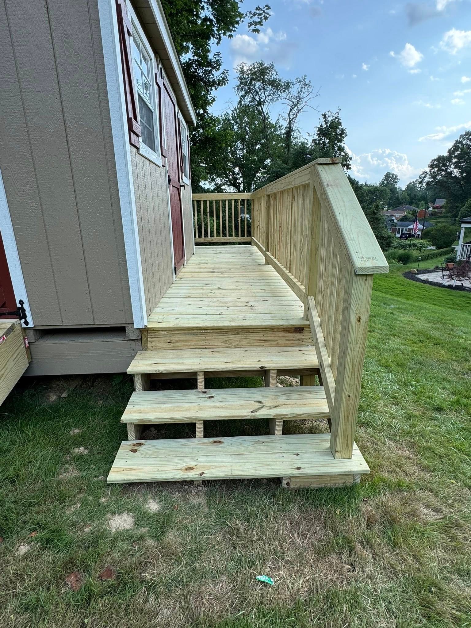 Wooden steps and ramp leading to the door of a beige shed with a red door and windows.