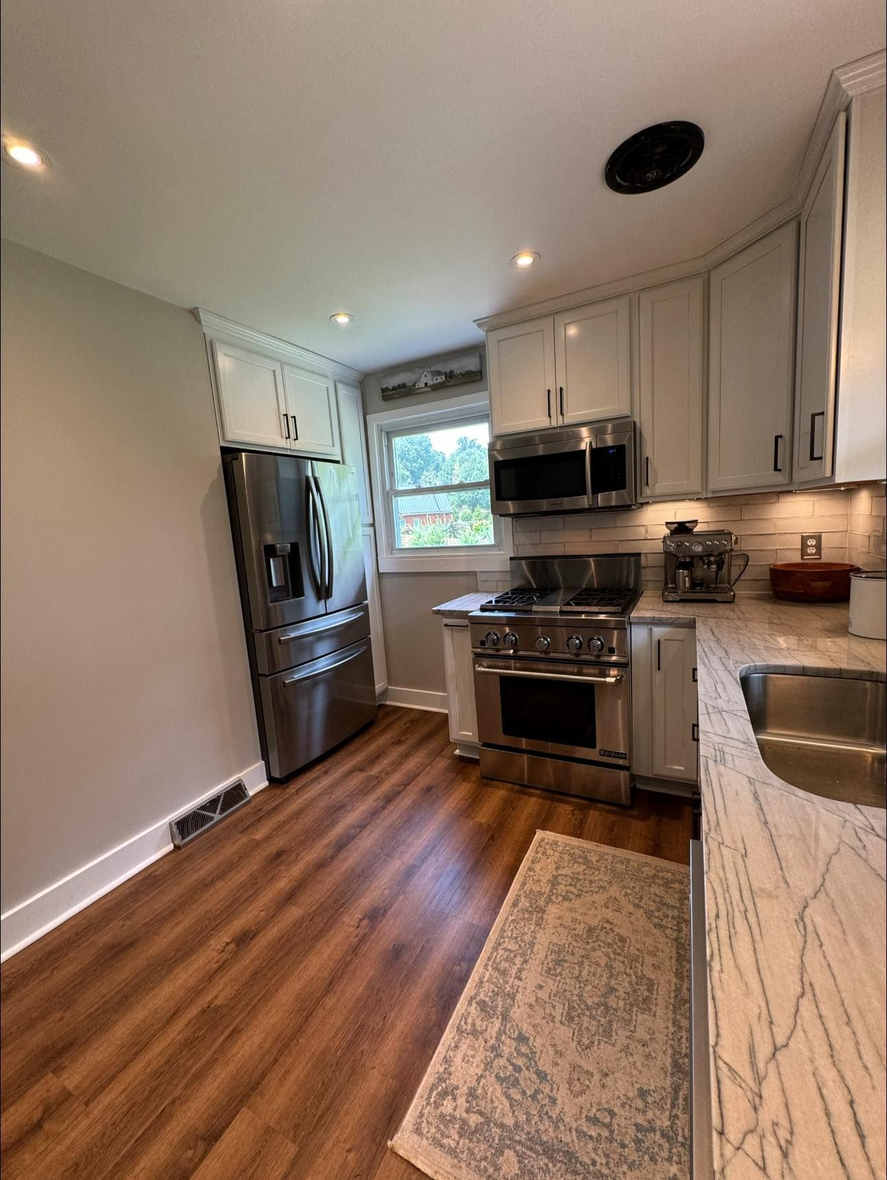 Kitchen with stainless steel appliances, white cabinets, and wood-look flooring.