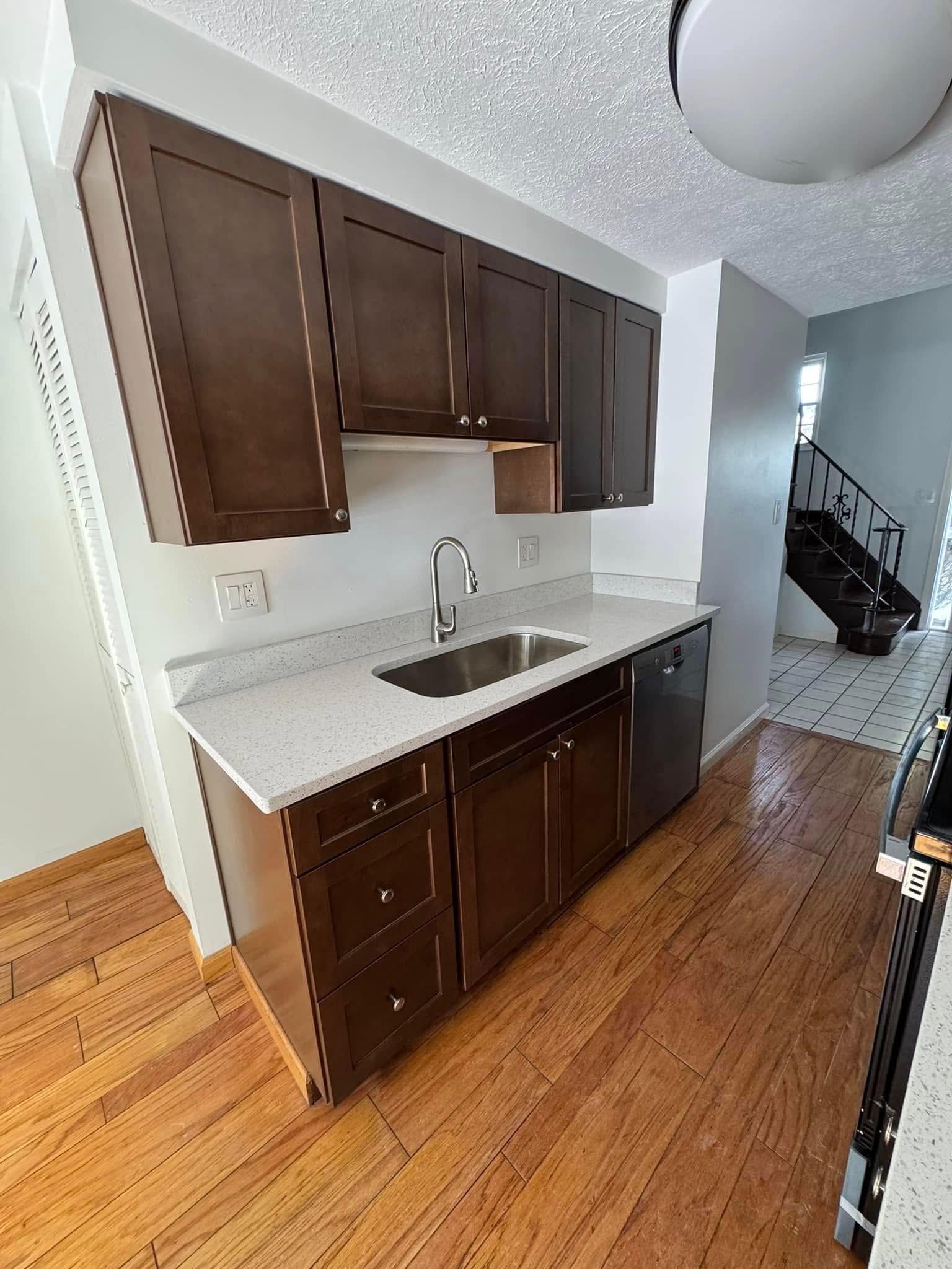 Kitchen with brown cabinets, white countertop, and a stainless steel sink, with a wooden floor.