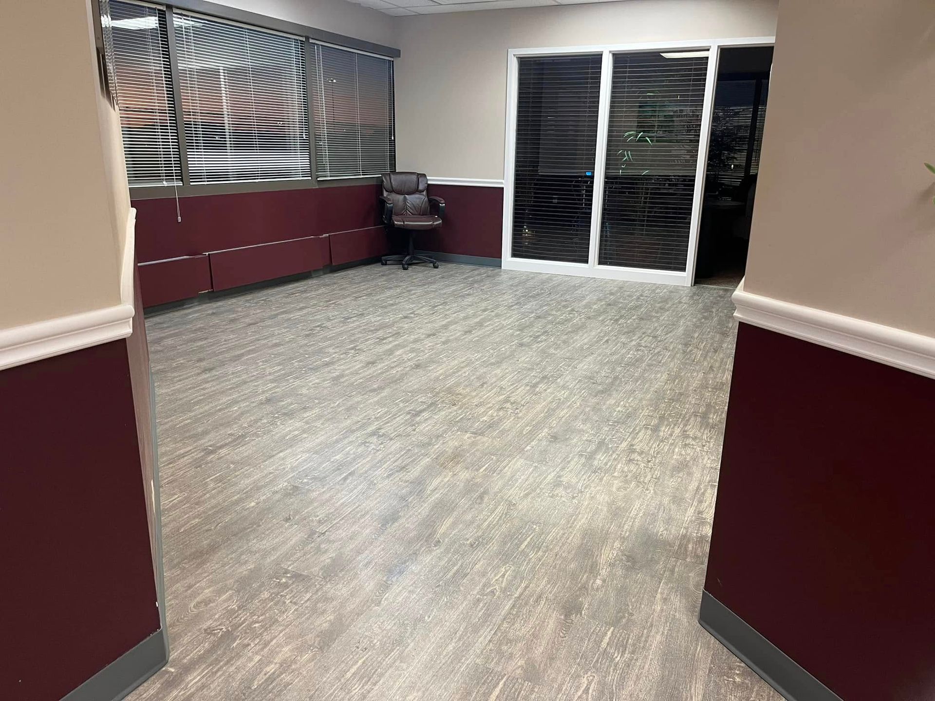 An empty office room with burgundy walls, blinds, and a door to the outside.