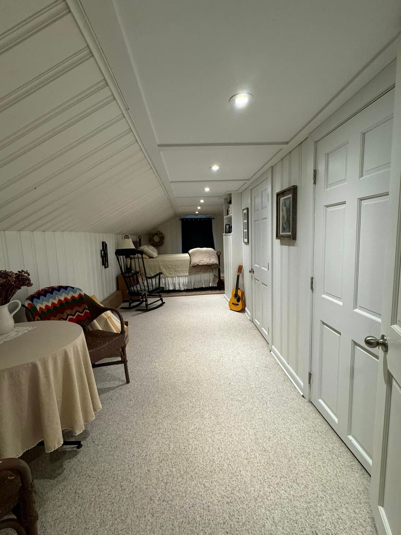 A long hallway with white paneling and doors, speckled floor, leading to beds, and a table with chairs.