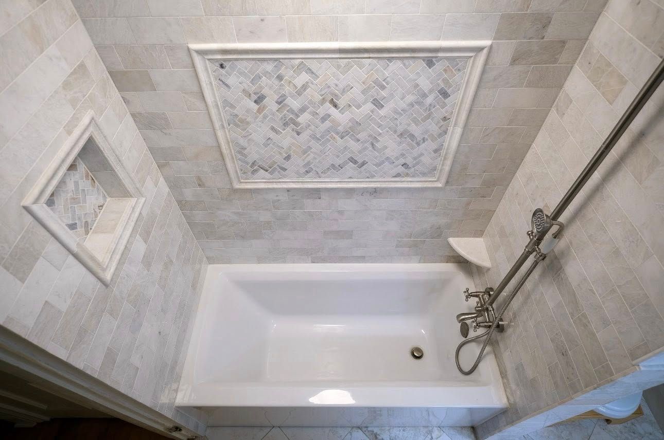 Bathroom with white bathtub, mosaic tile accent, and shower fixtures.