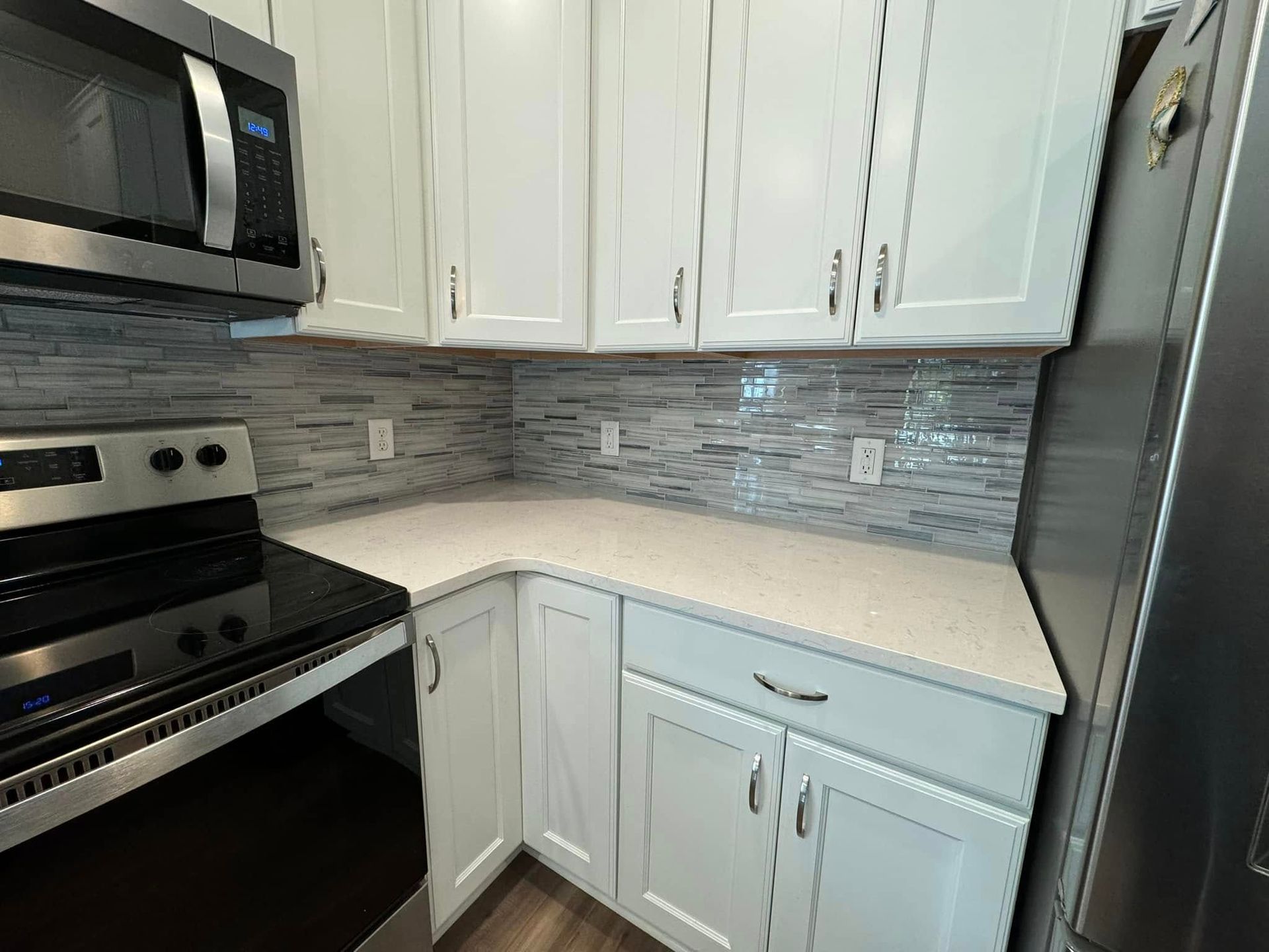 White kitchen cabinets with white countertops, stainless steel appliances, and a tiled backsplash.