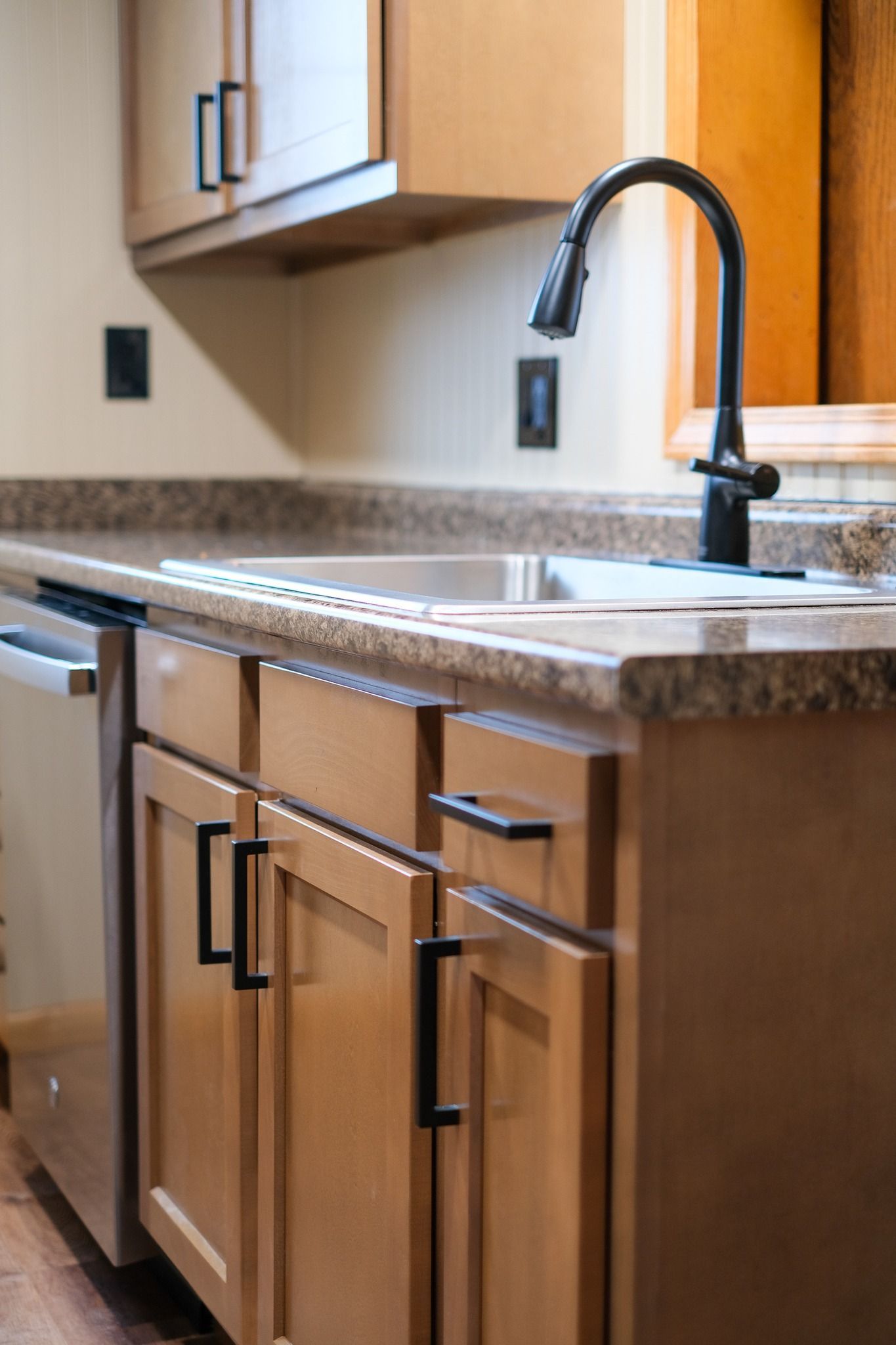 Kitchen with light-brown cabinets, stainless steel sink, black faucet, and dishwasher.