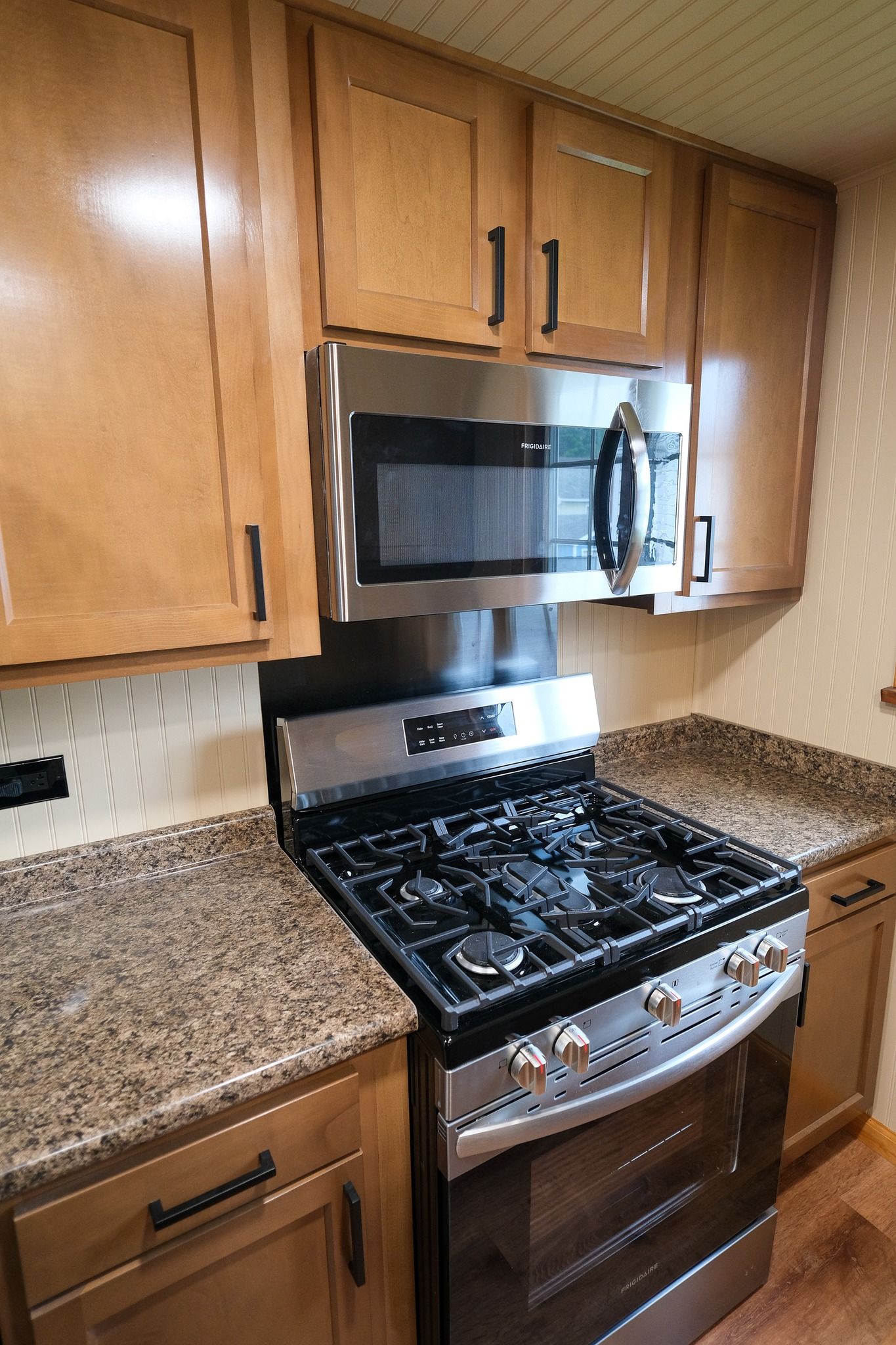 Stainless steel oven and microwave in a kitchen with tan cabinets and speckled countertops.