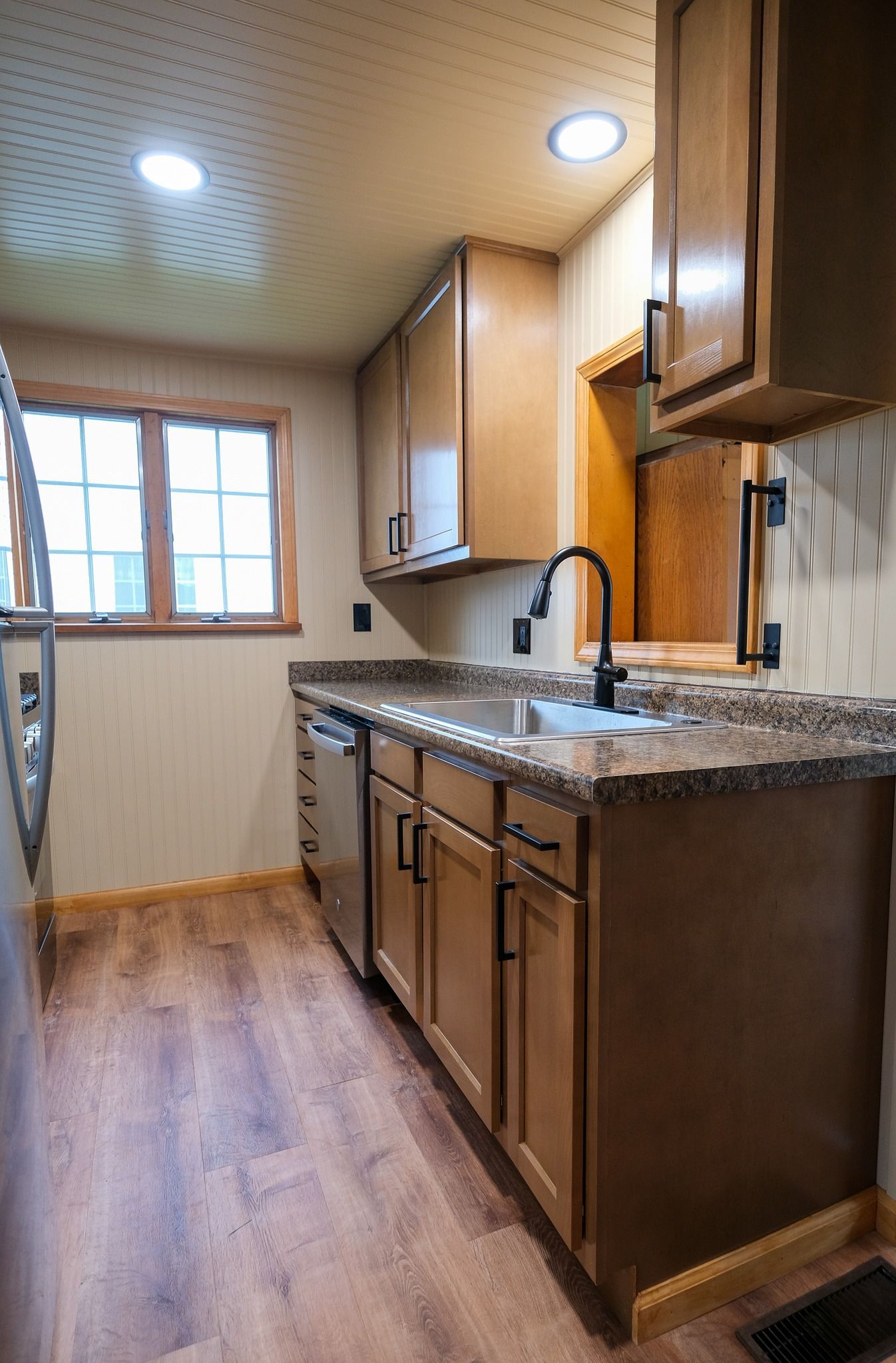Kitchen with light brown cabinets, dark countertop, and wood-look flooring. Window with natural light.