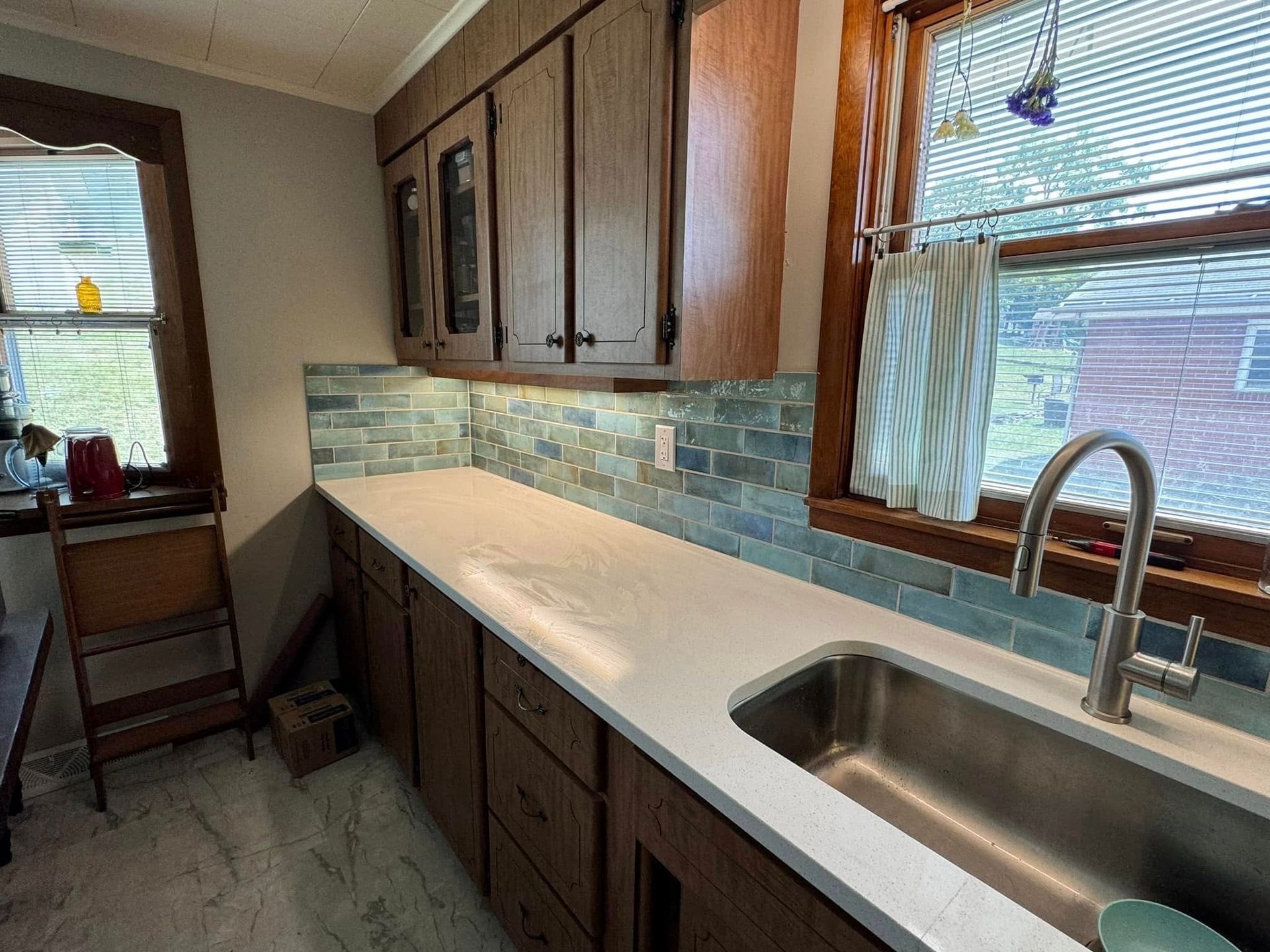 Kitchen with light countertops, blue tile backsplash, wooden cabinets, and a window.