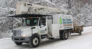 A white truck with a crane on top of it is driving down a snowy road.