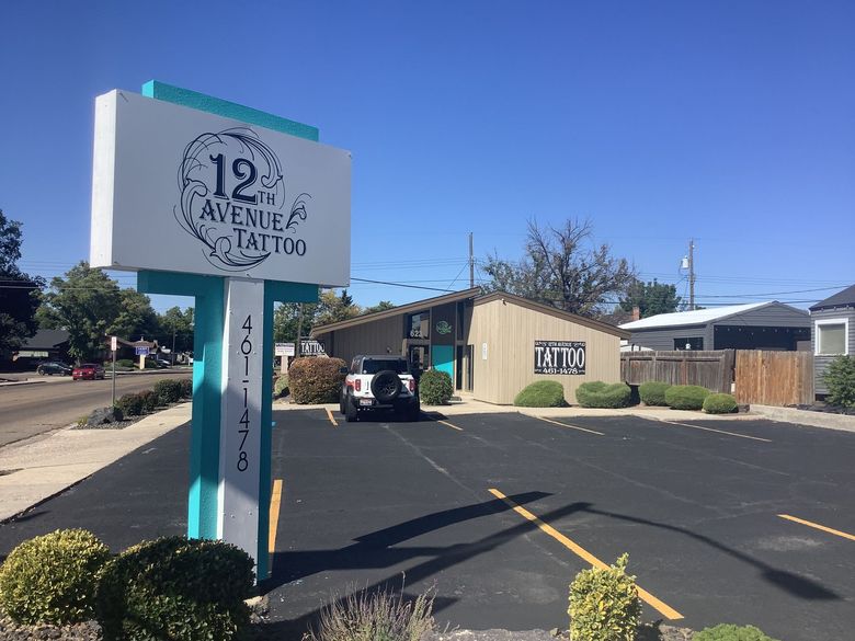 Sign for 12th Avenue Tattoo shop in front of the building with a car parked in the parking lot.
