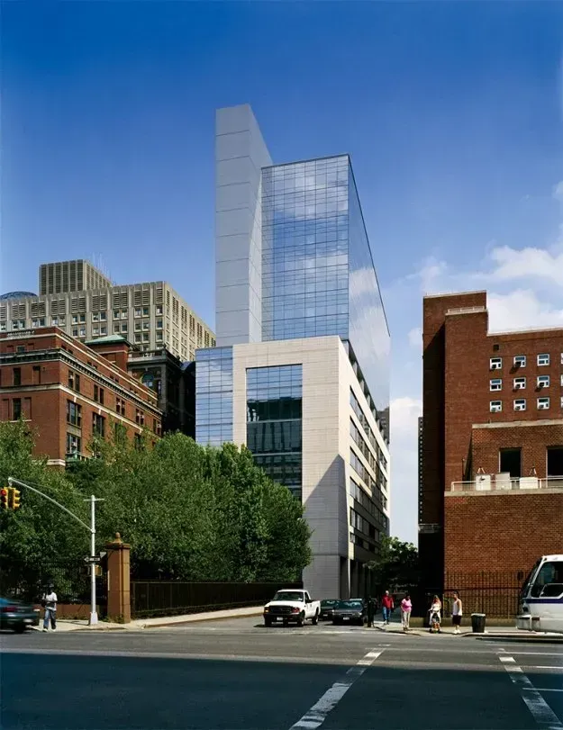Modern glass high-rise rising above older brick buildings on a city street under a blue sky
