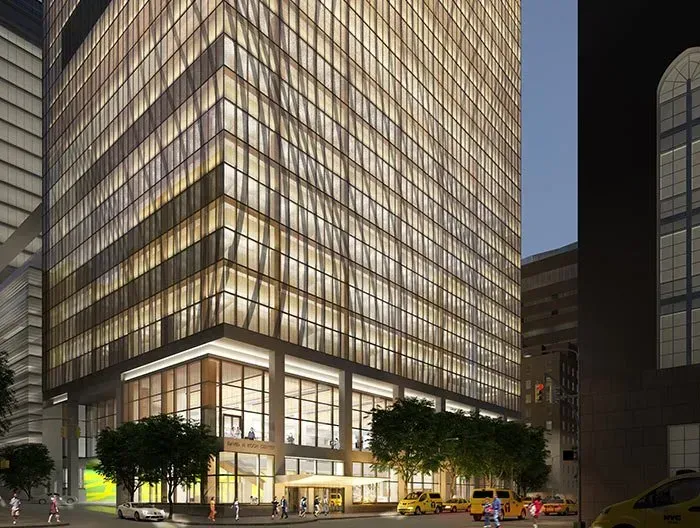 Illuminated glass office tower at dusk with street-level trees and cars below