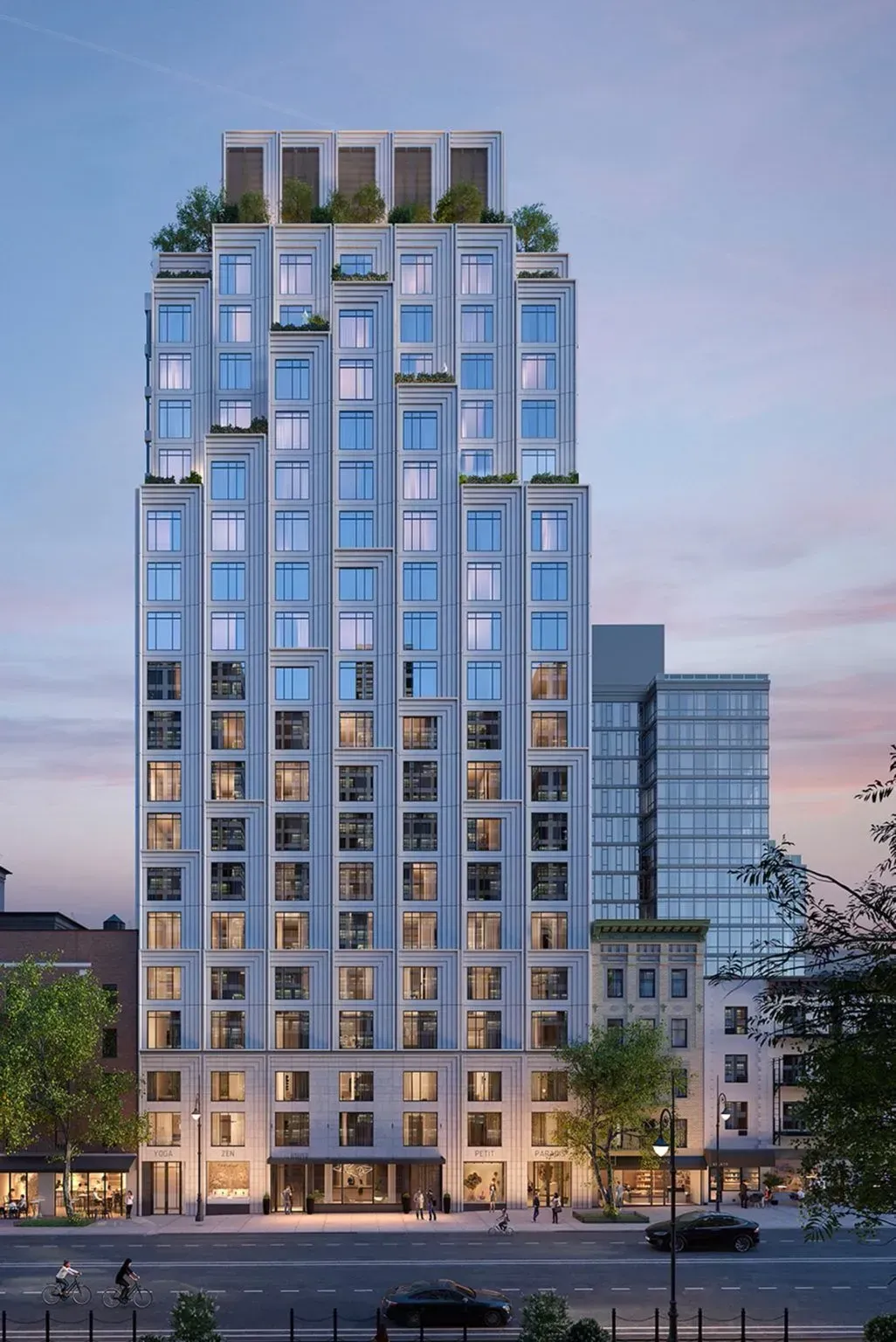 Tall modern apartment building with many lit windows at dusk under a pink-blue sky