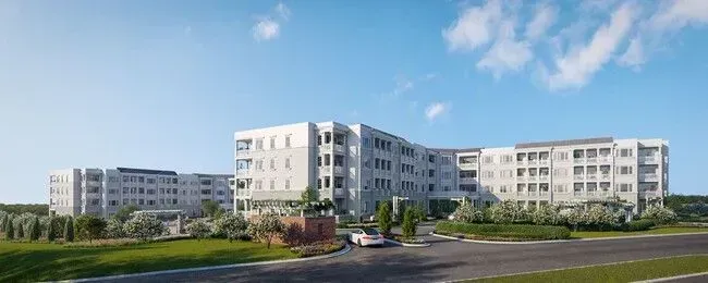 Modern white apartment buildings along a landscaped road under a clear blue sky