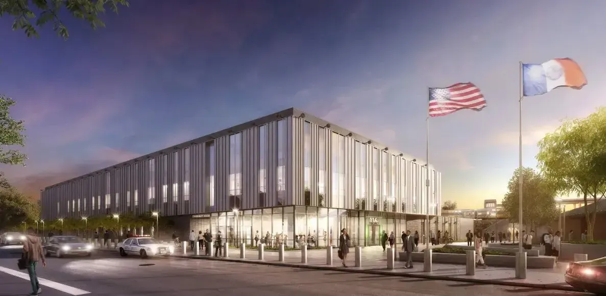 Modern glass office building at dusk with flags, lit windows, and people gathered outside
