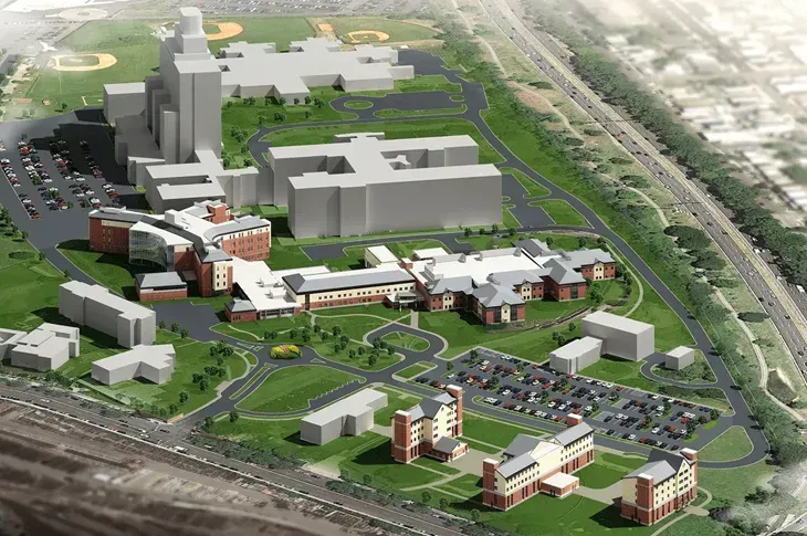 Aerial rendering of a campus with buildings, roads, parking, and landscaped green spaces beside a rail line