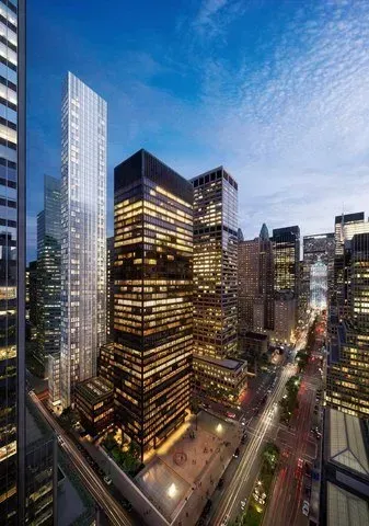 Tall modern office towers lit at dusk in a dense city skyline under a blue sky