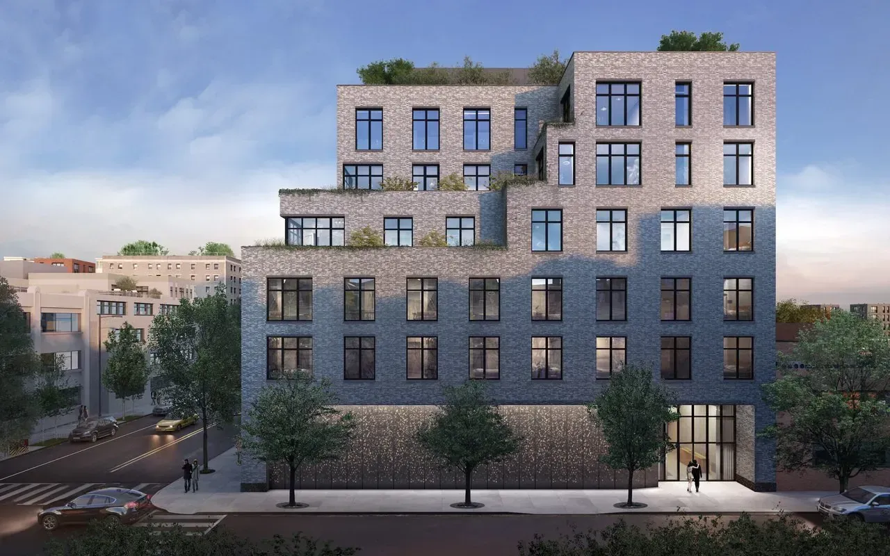 Modern gray brick apartment building with rooftop terraces and street-level storefronts at dusk
