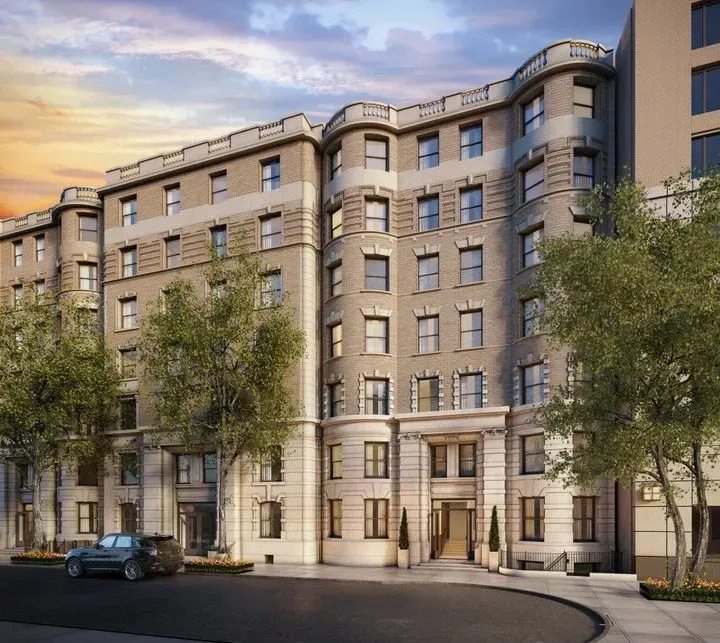Elegant beige stone apartment building with curved facade, trees, parked car, and sunset sky