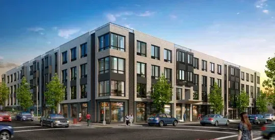 Modern apartment building on a city street with cars, trees, and pedestrians at dusk