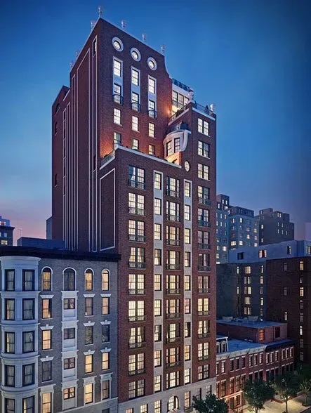 Tall brick apartment building with lit windows at dusk in a city skyline