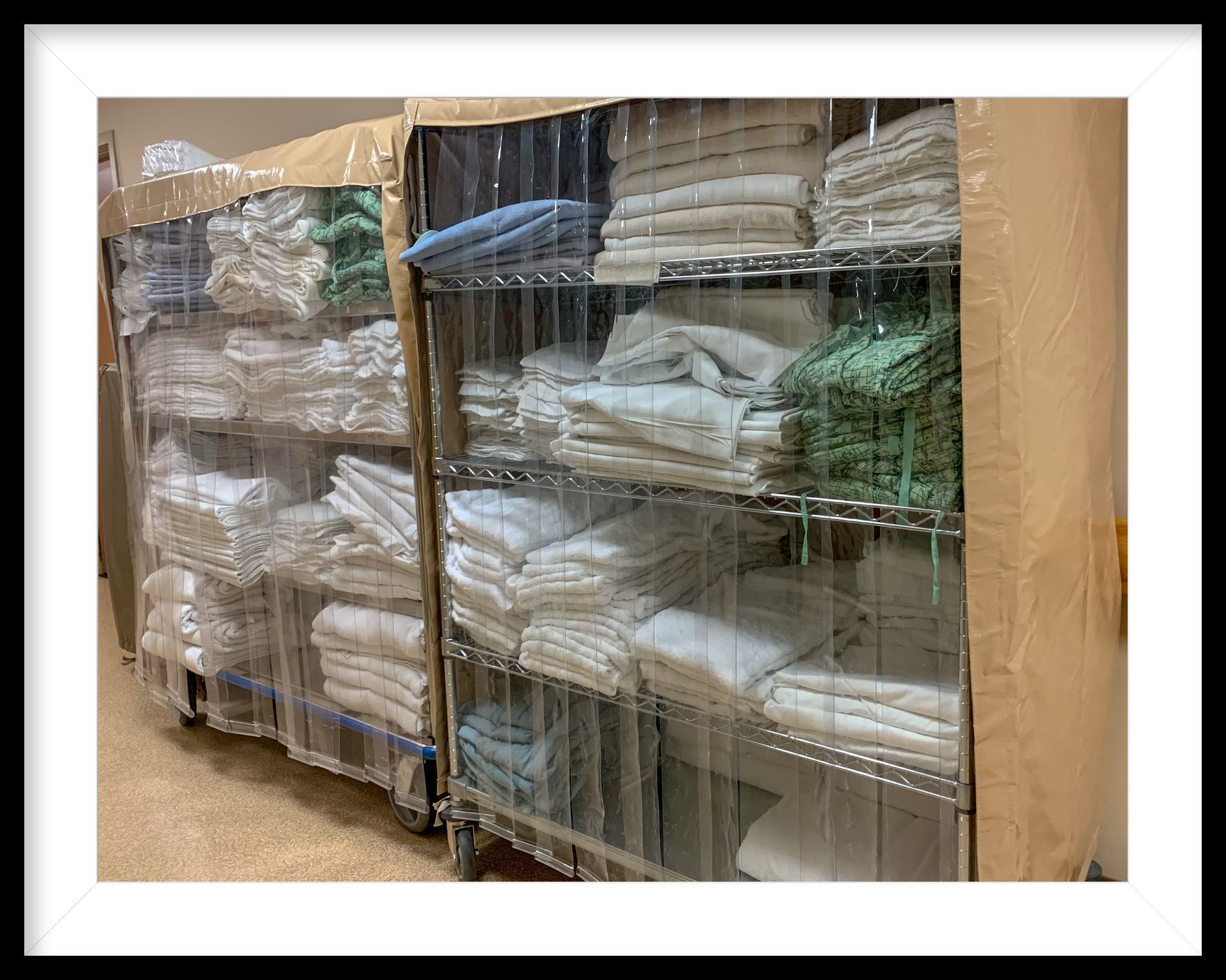 Two metal shelving units on wheels, stocked with folded linens and enclosed by clear plastic curtains.