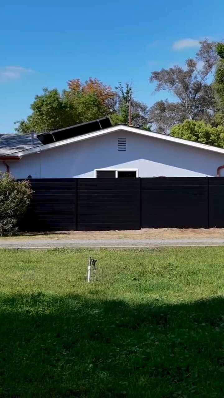 Black fence in front of a light blue house under a clear blue sky with a solar panel on the roof.