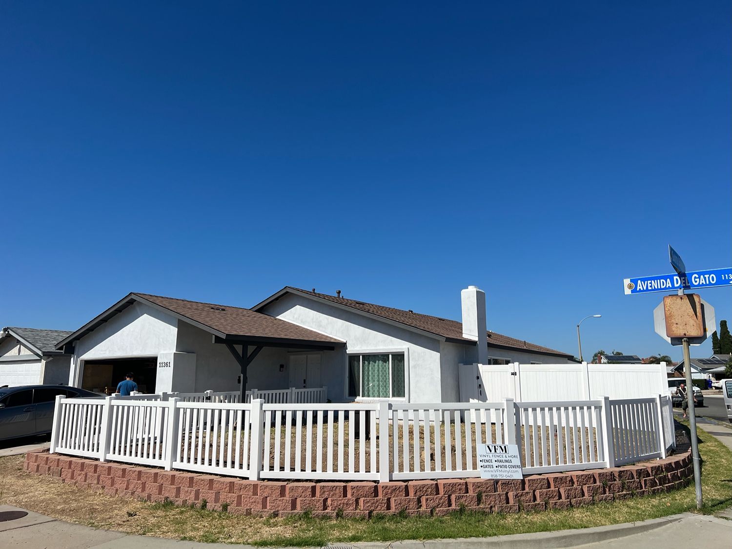 White house with picket fence on a corner lot, blue sky overhead.