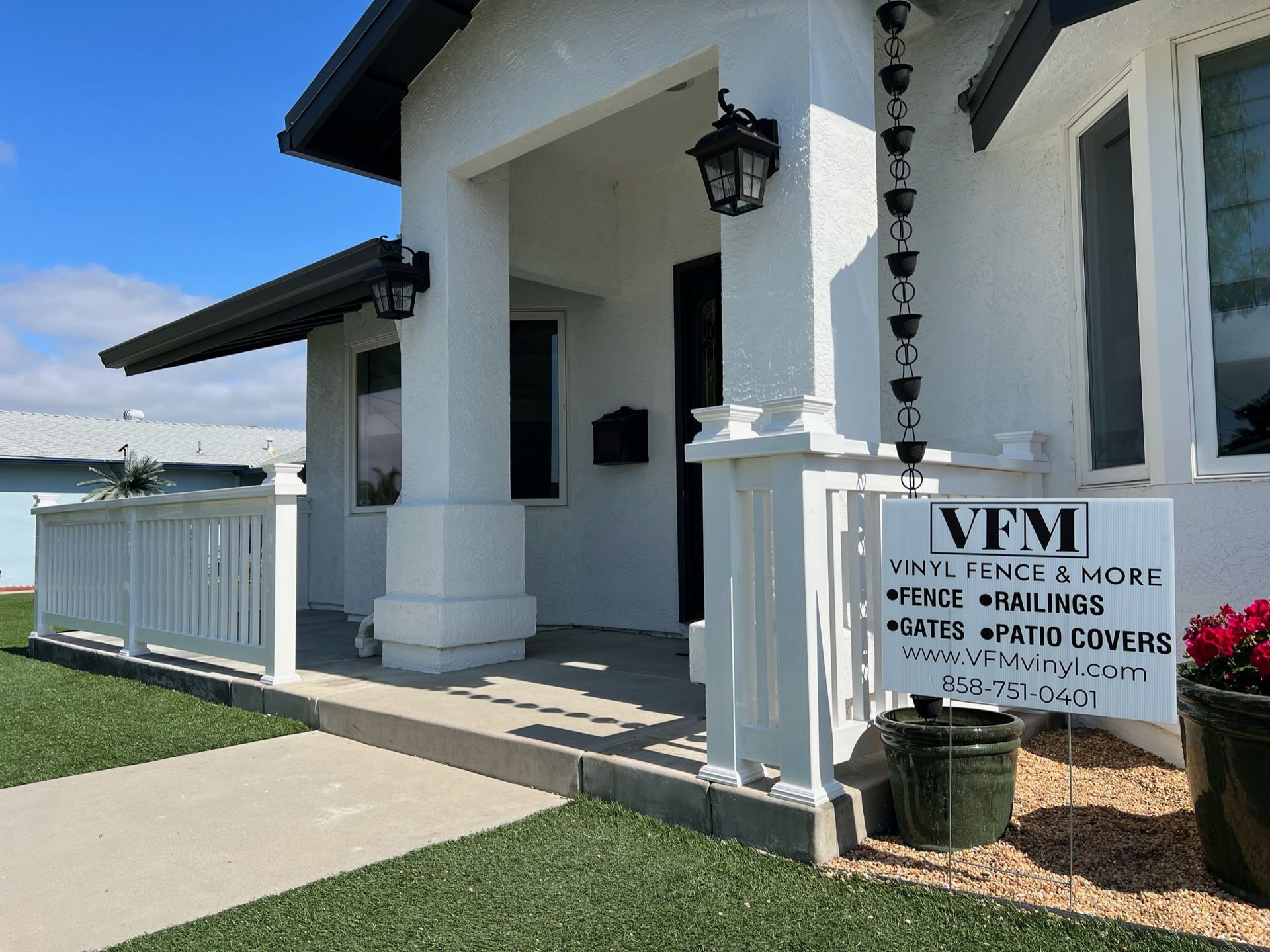 White house with porch, railing, and sign for Vinyl Fence & More. Sunny day.