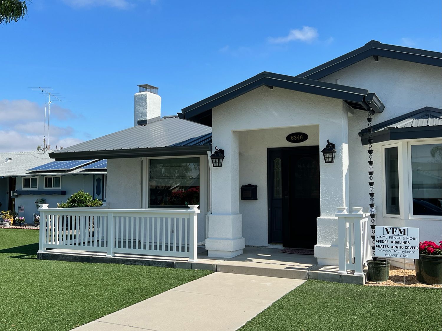 White house with black trim, blue sky. Porch with white railing and black door, green grass.