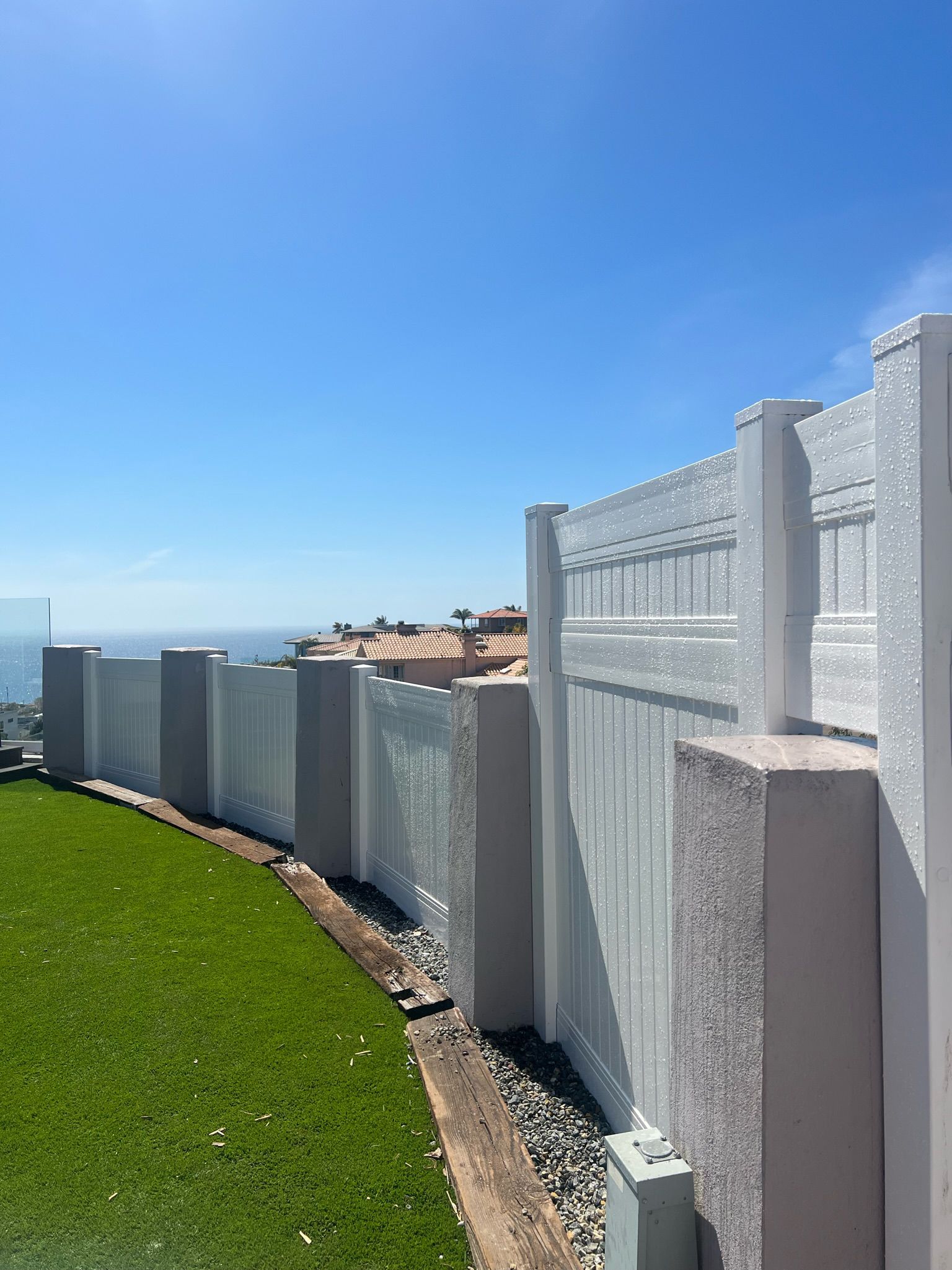 White decorative fence with ocean view and green grass under a blue sky.